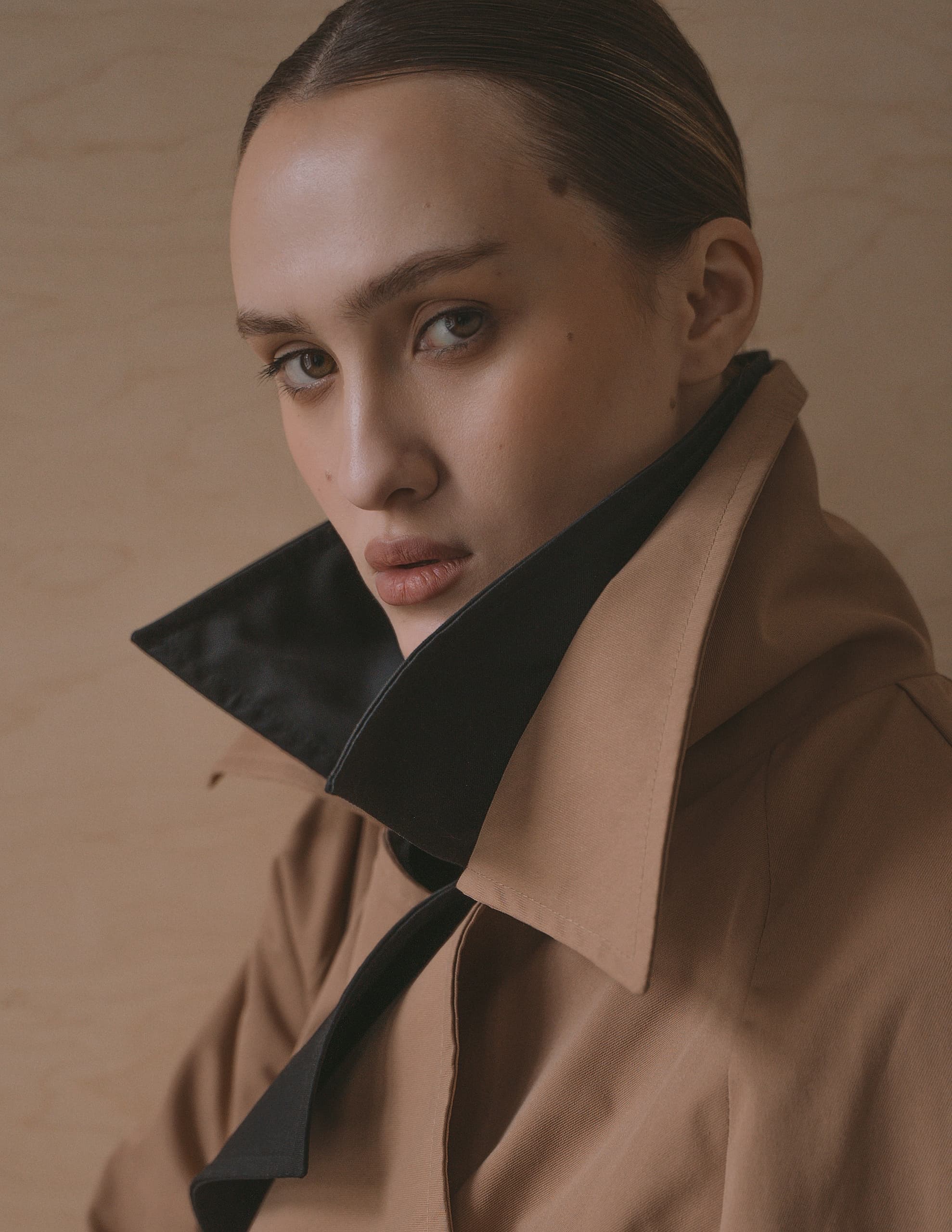 Portrait of a person in a beige coat with a high collar, neutral background.