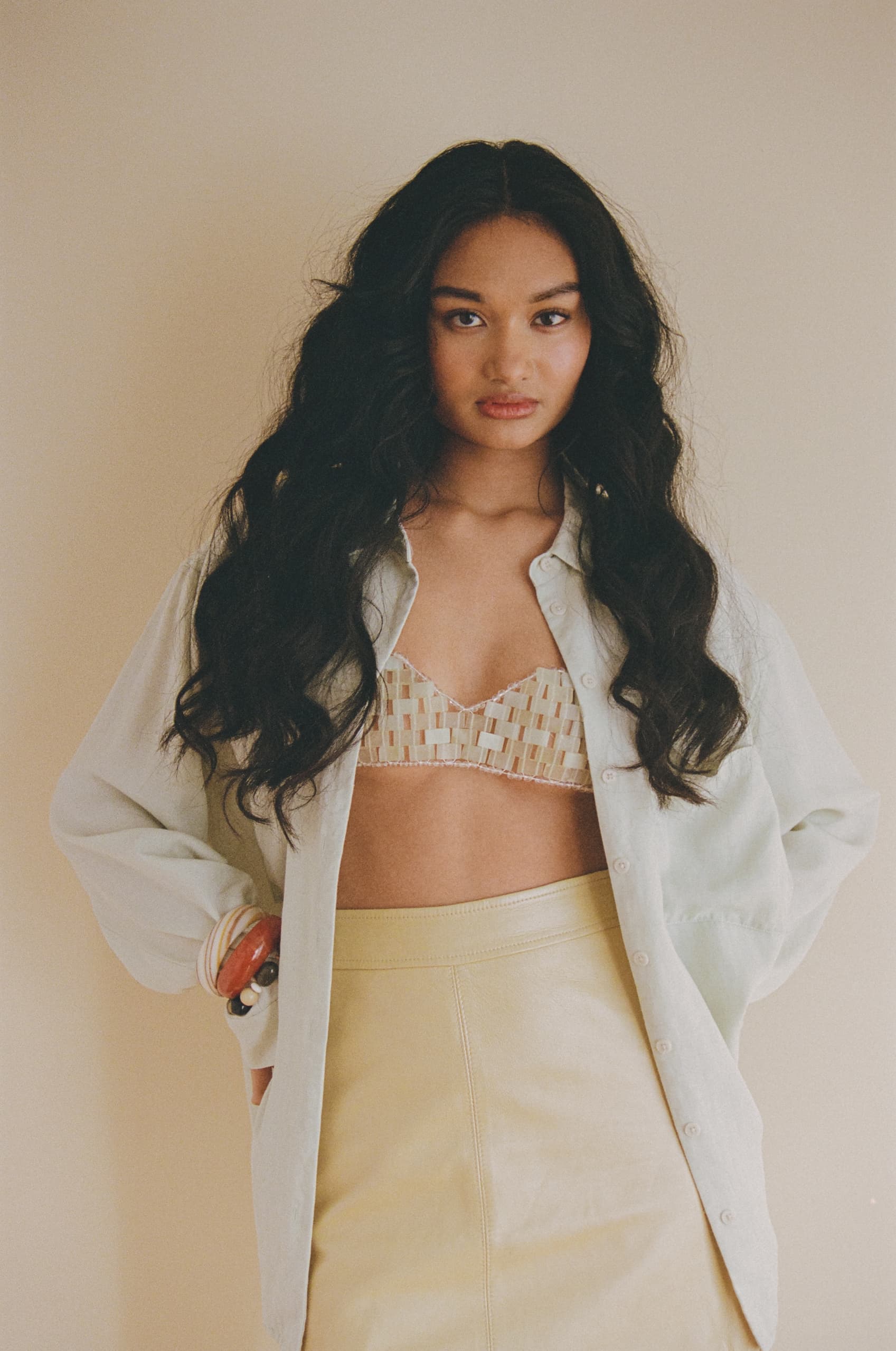 Woman in stylish shirt and skirt with long hair, posing confidently indoors.