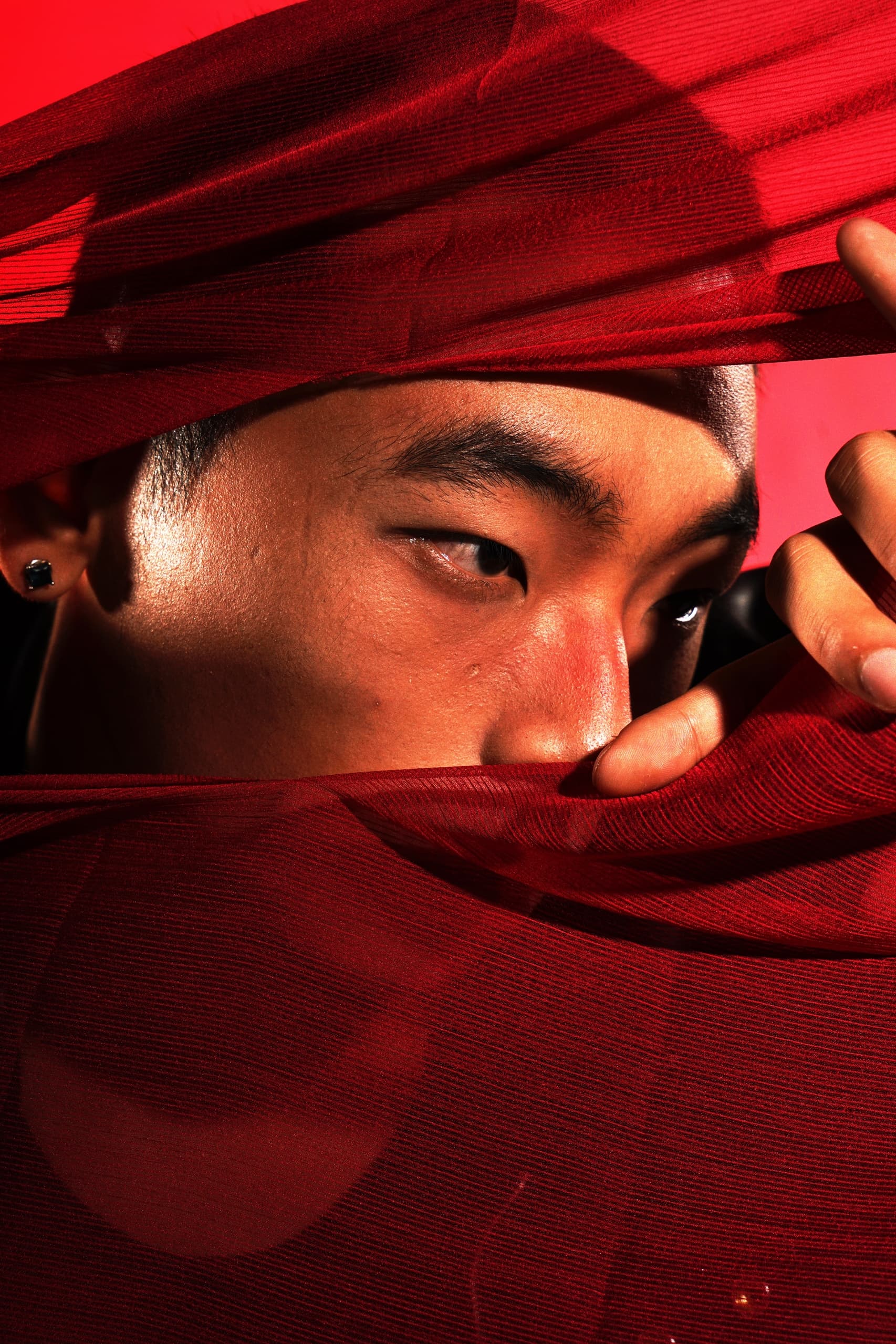Mysterious gaze through vibrant red fabric, creating an alluring and enigmatic look.
