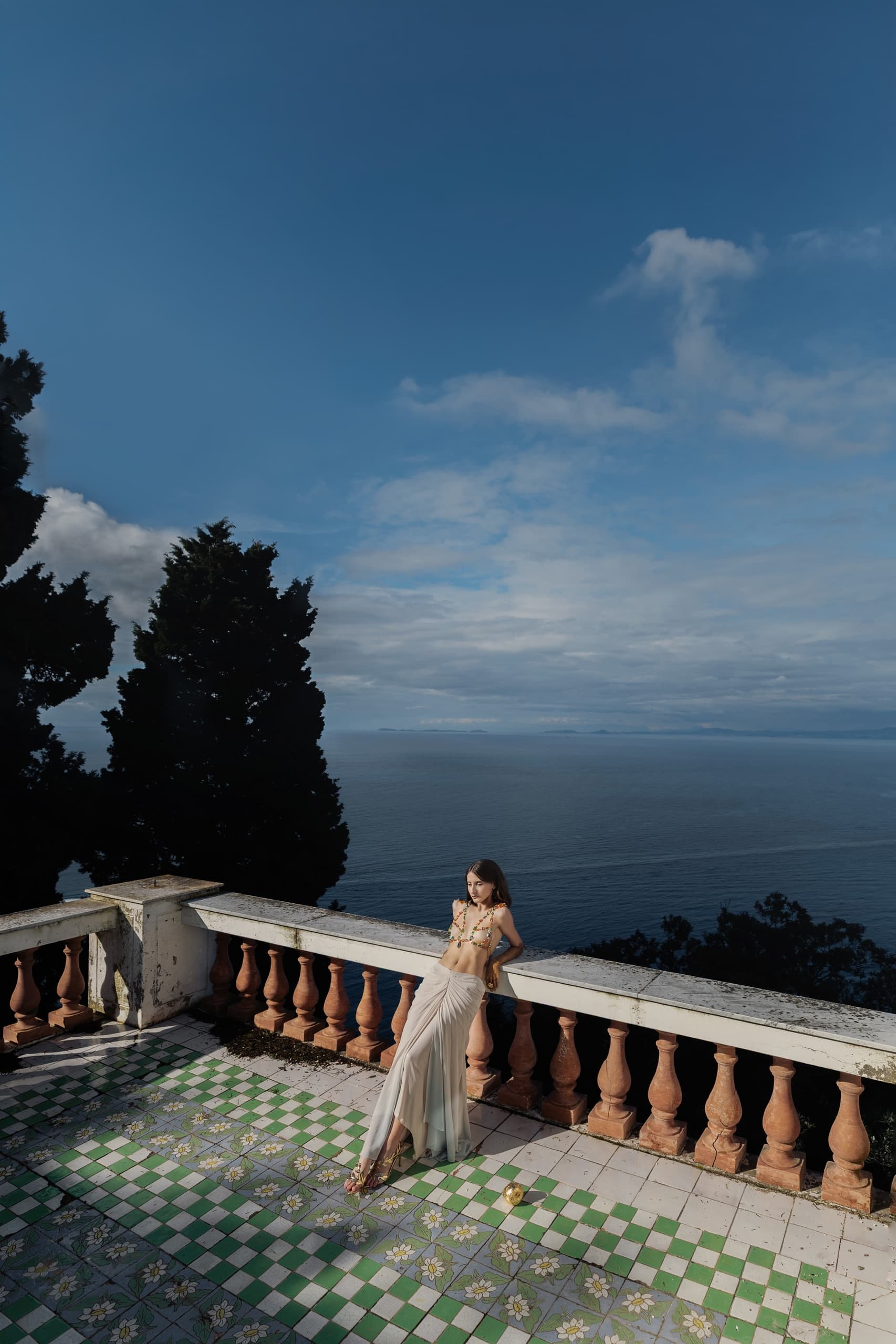 Woman in stylish outfit on a terrace overlooking the ocean under a clear sky.