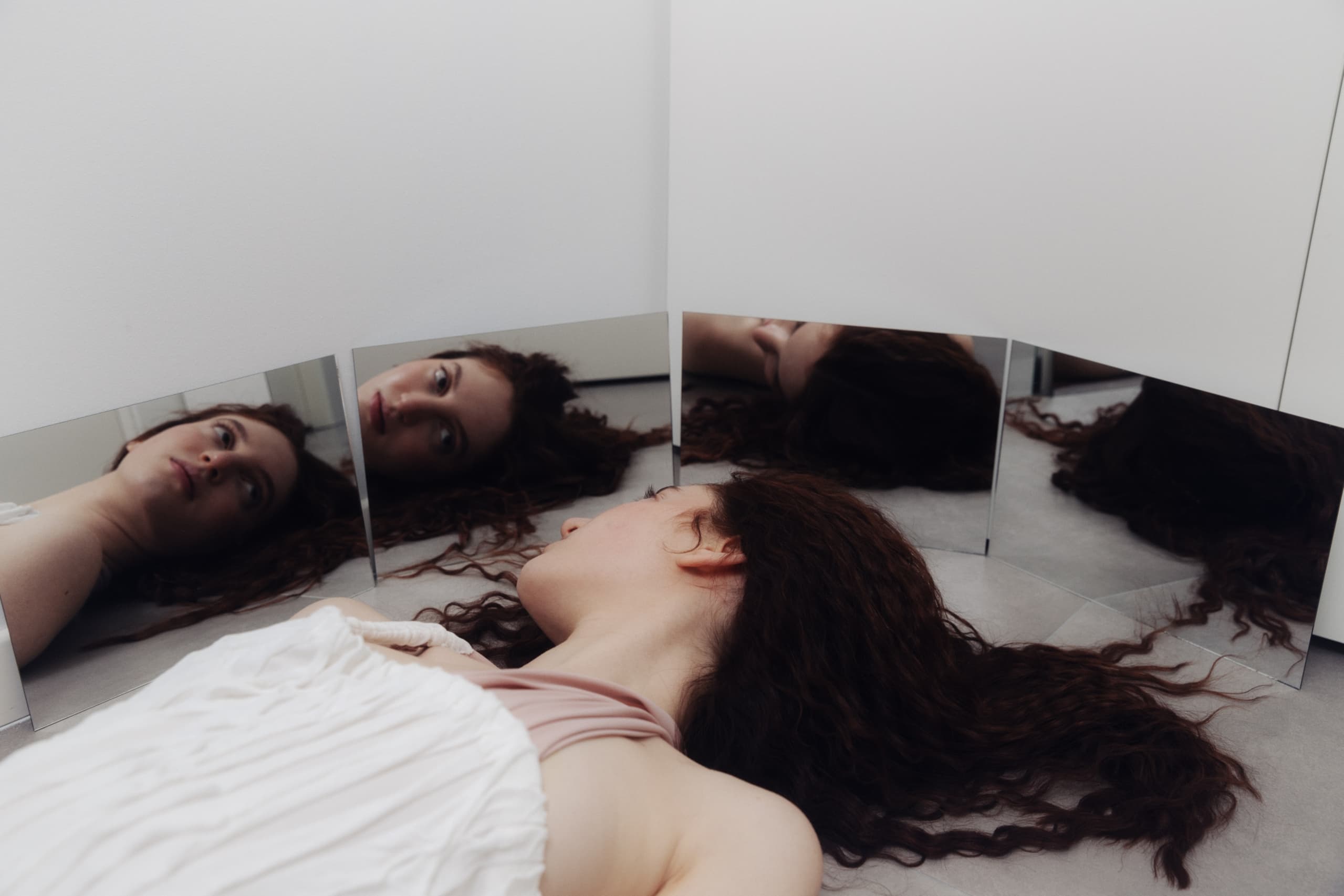 Woman with curly hair reflected in multiple mirrors, laying on the floor.