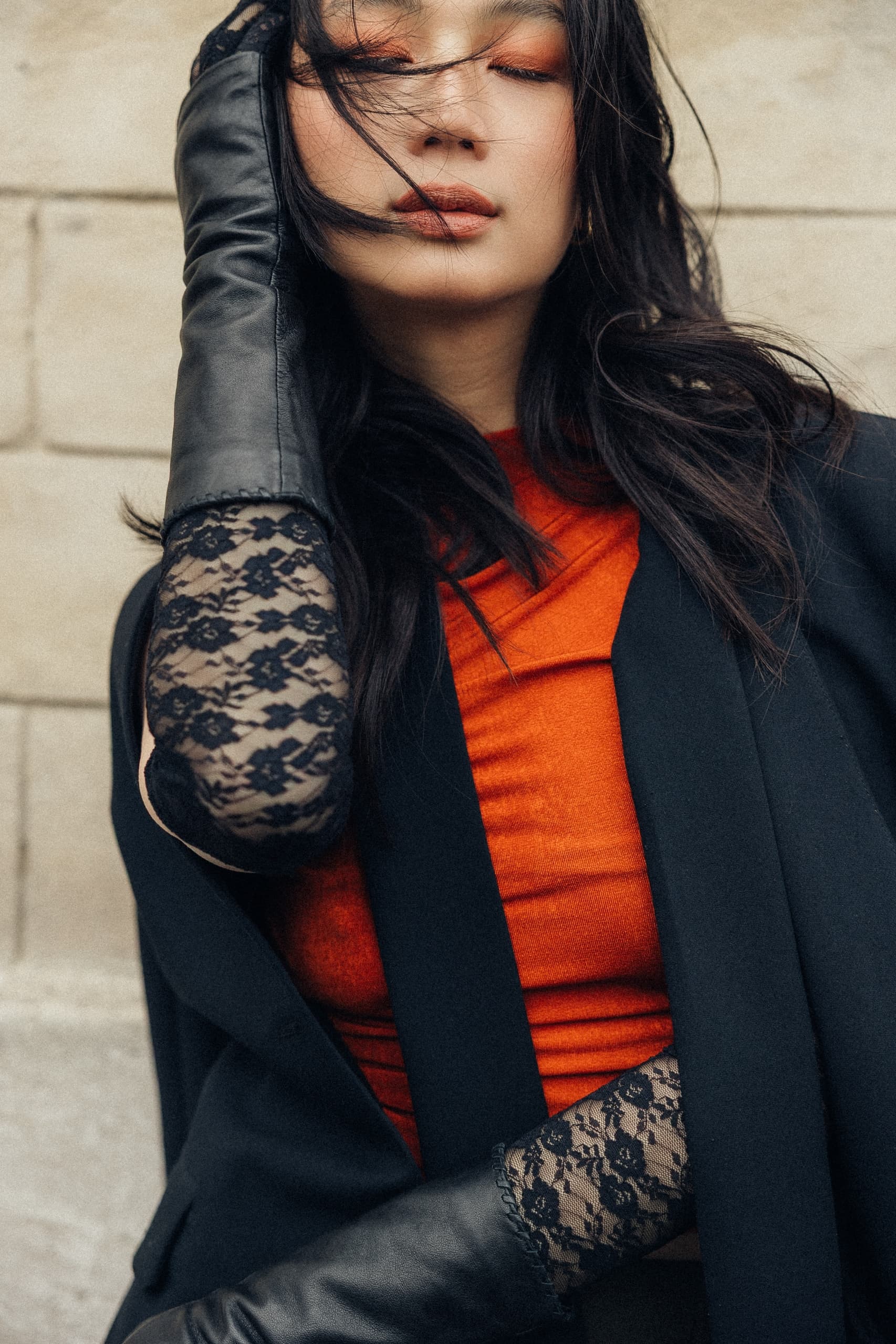 Stylish woman in red and black with lace gloves poses against a stone wall.