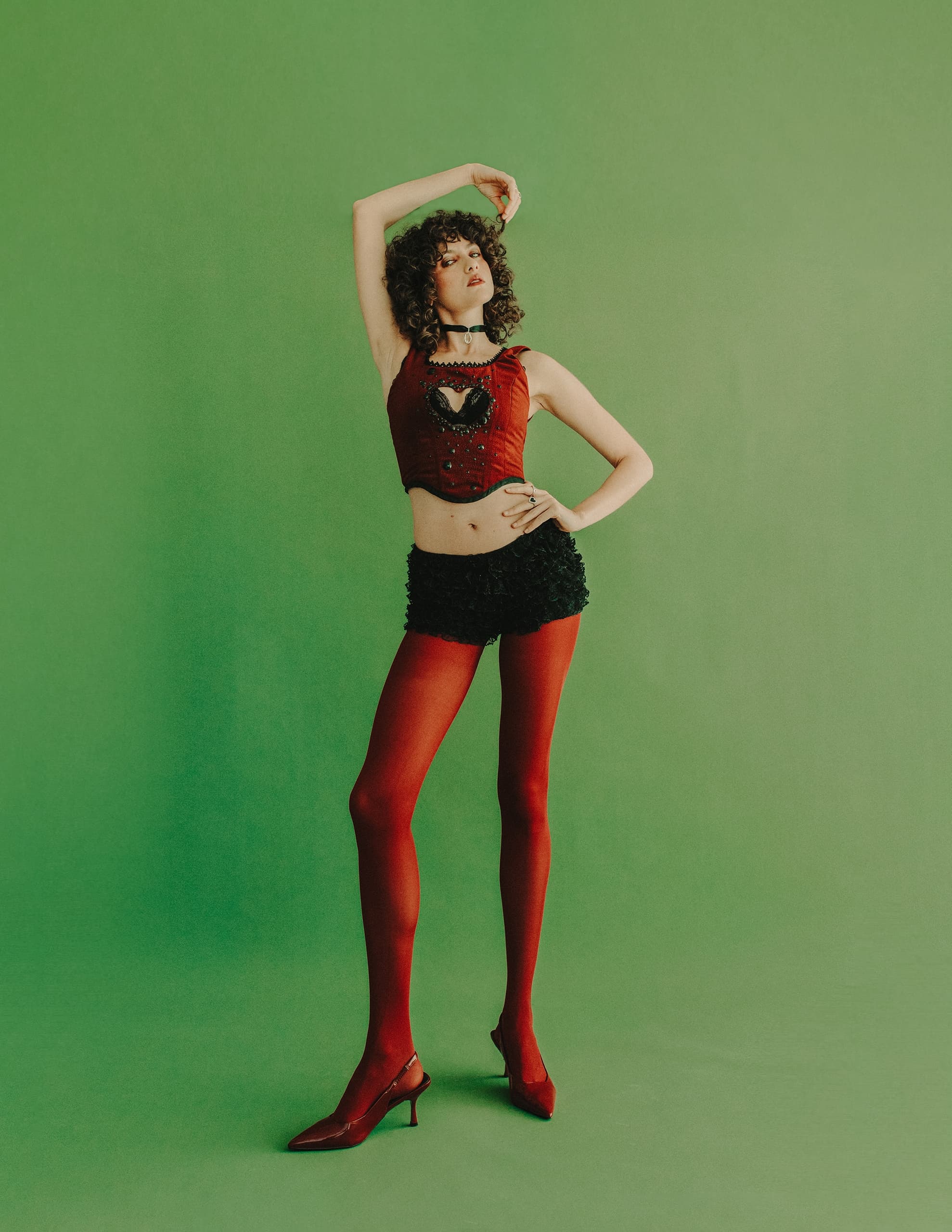 Fashionable person in red outfit posing against a green background.