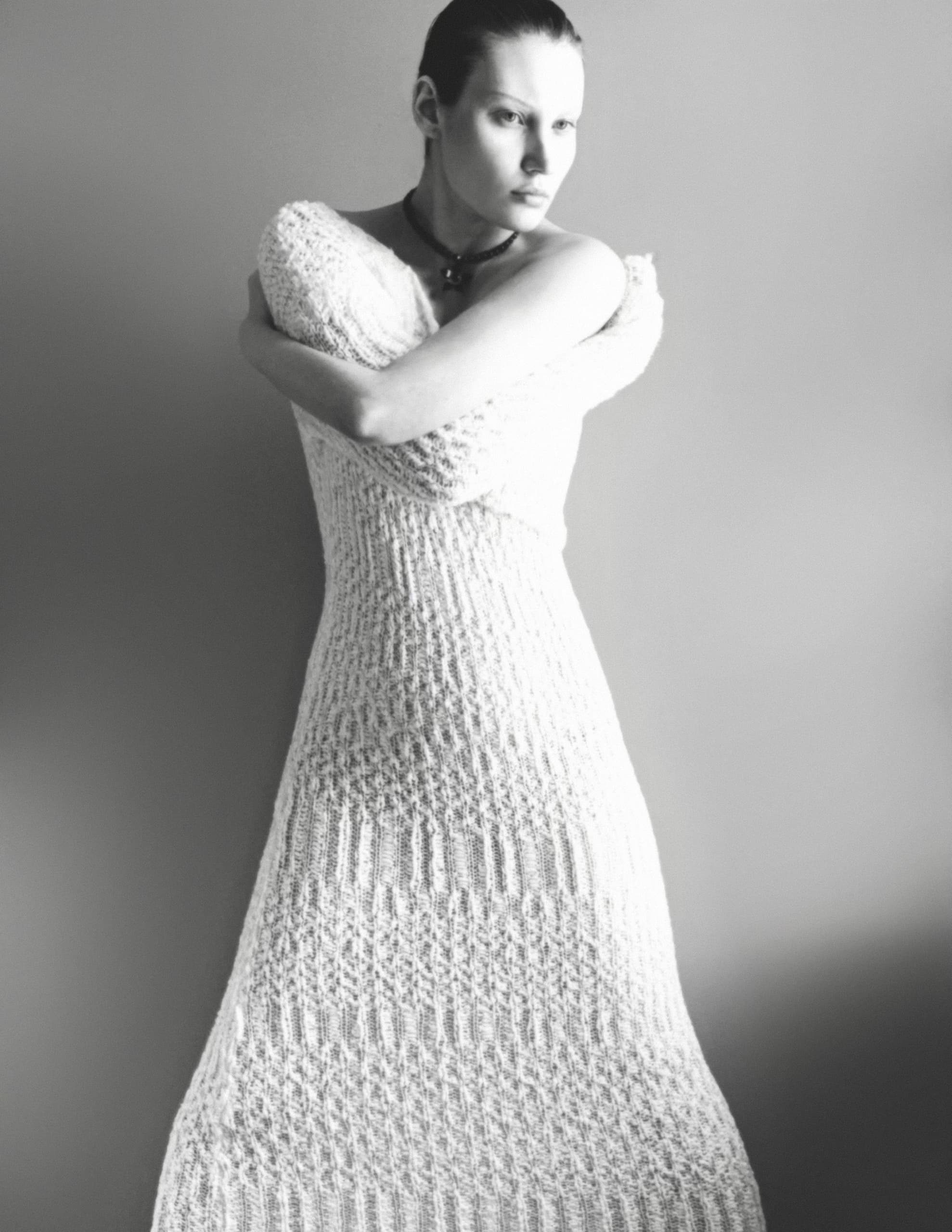 Monochrome portrait of a person in a knitted dress against a plain background.