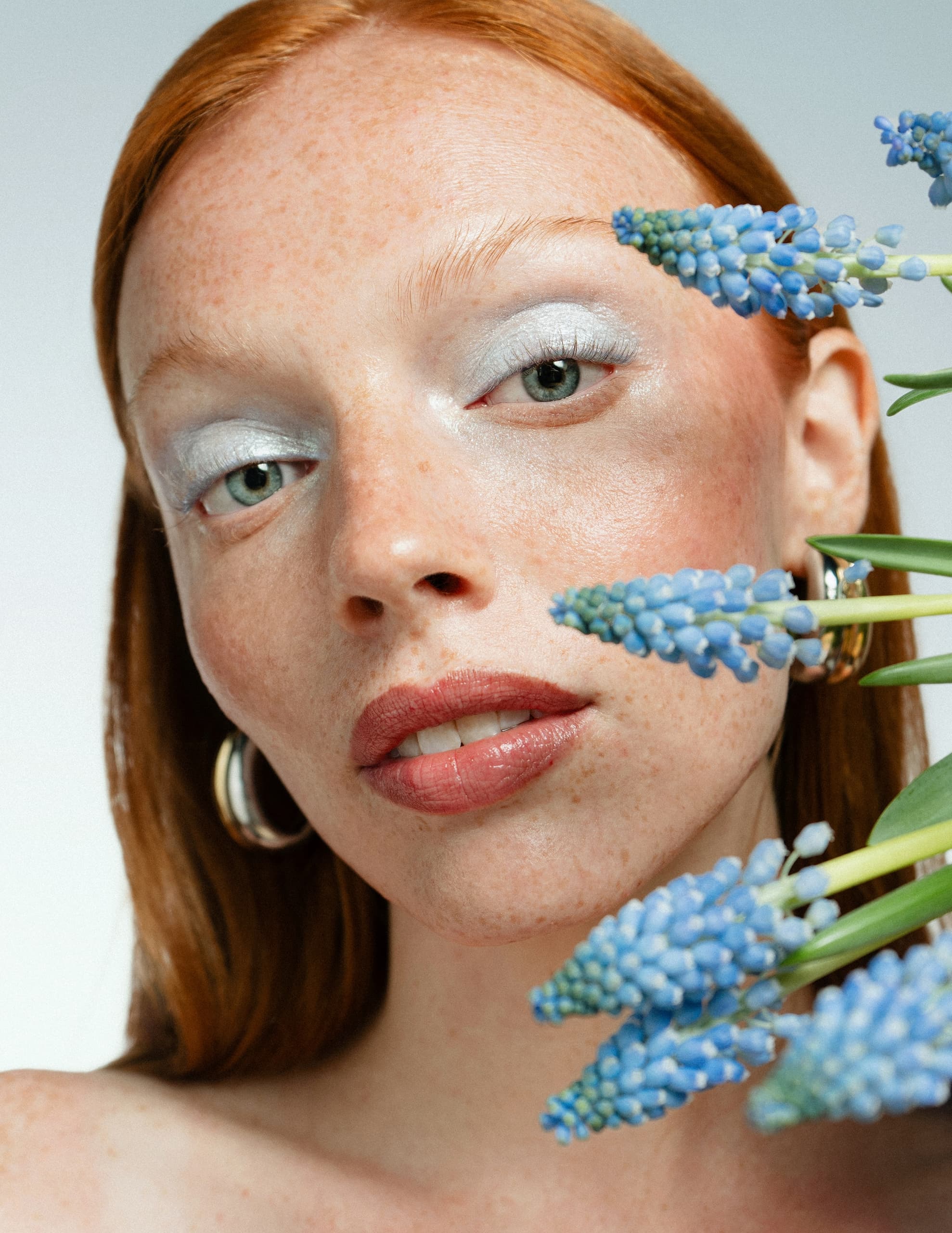 Close-up of woman with red hair and blue flowers for a fresh, natural look.