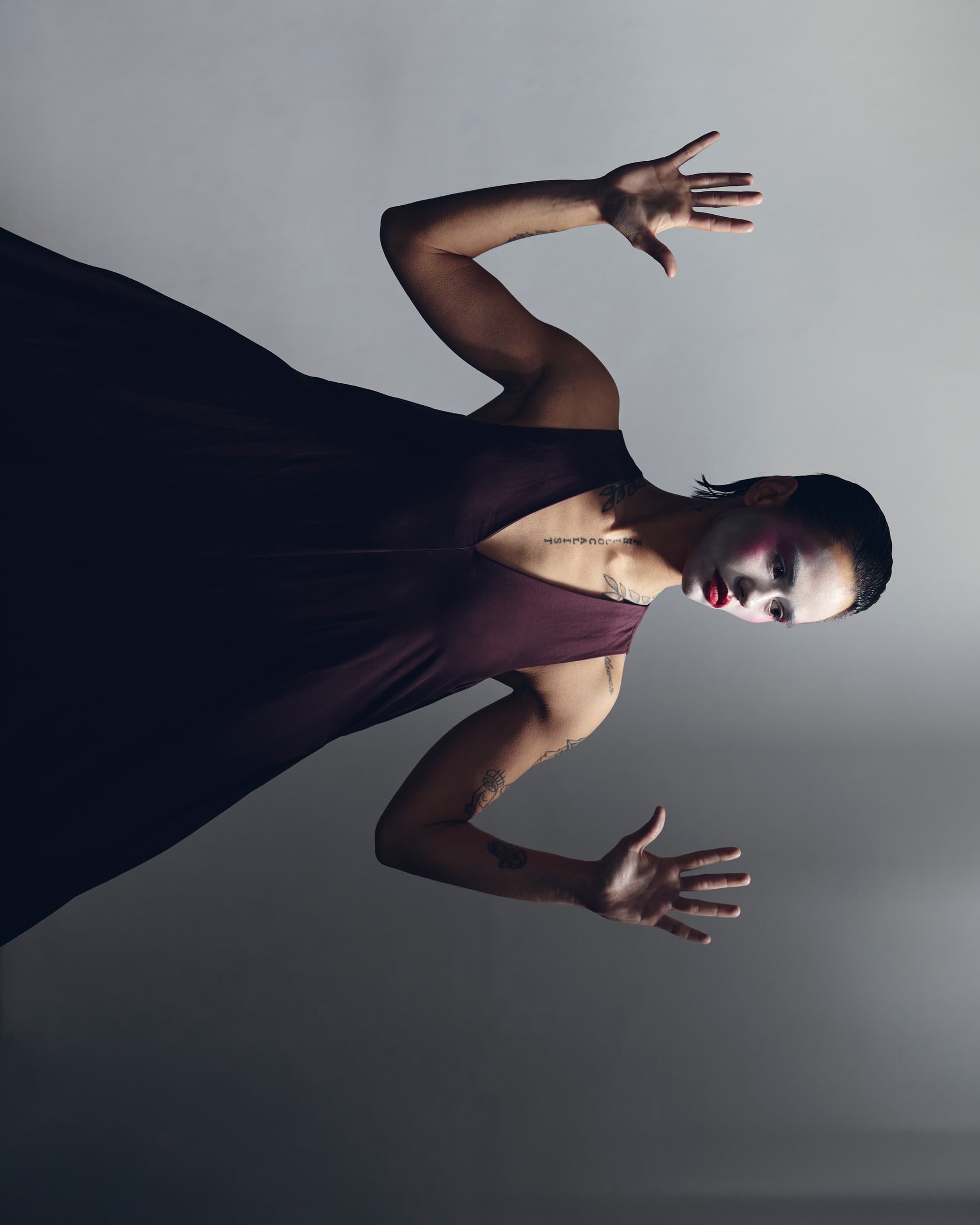 Person with dramatic makeup in dark dress, posing creatively against gray background