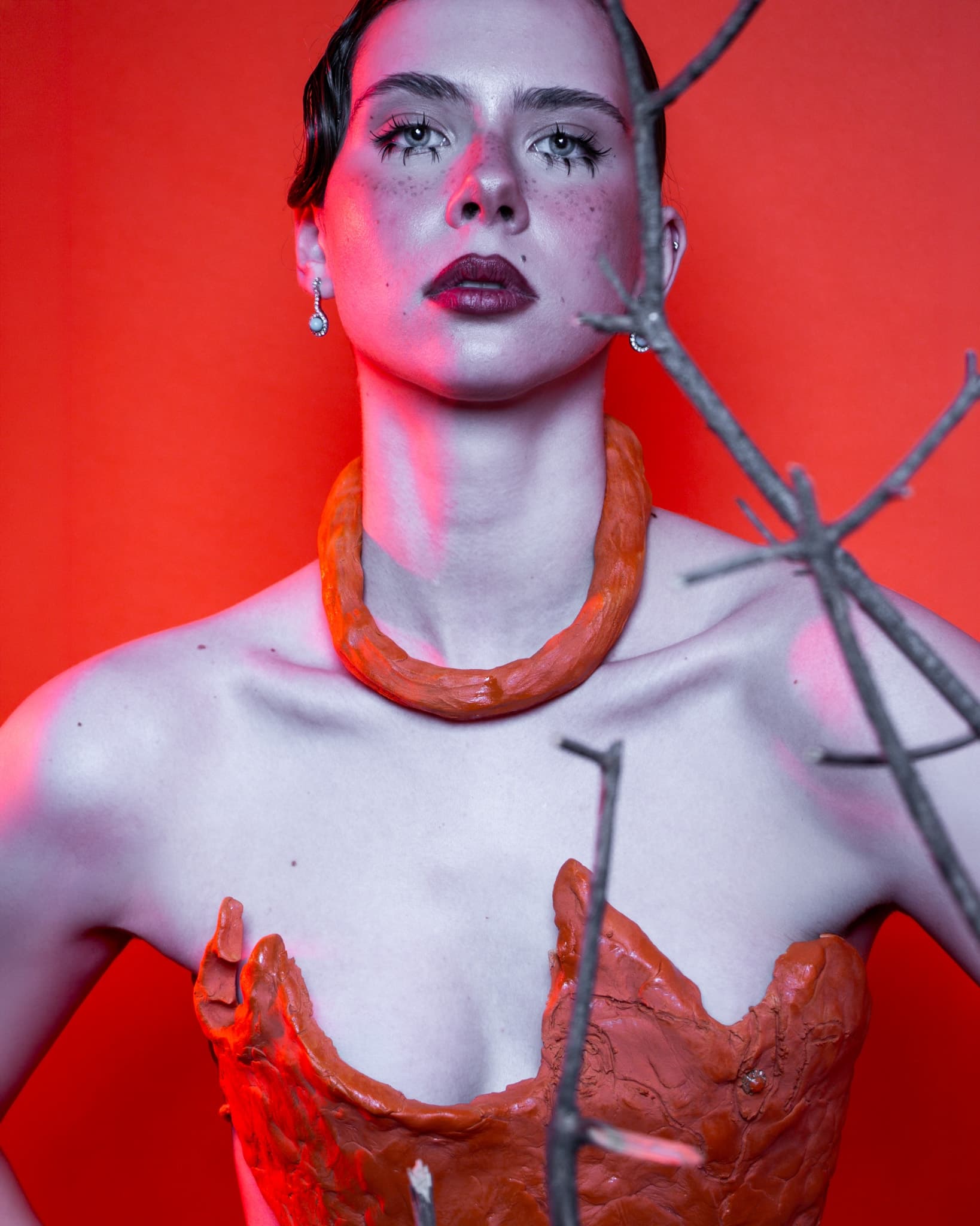 Avant-garde fashion portrait with red clay outfit and dramatic makeup.