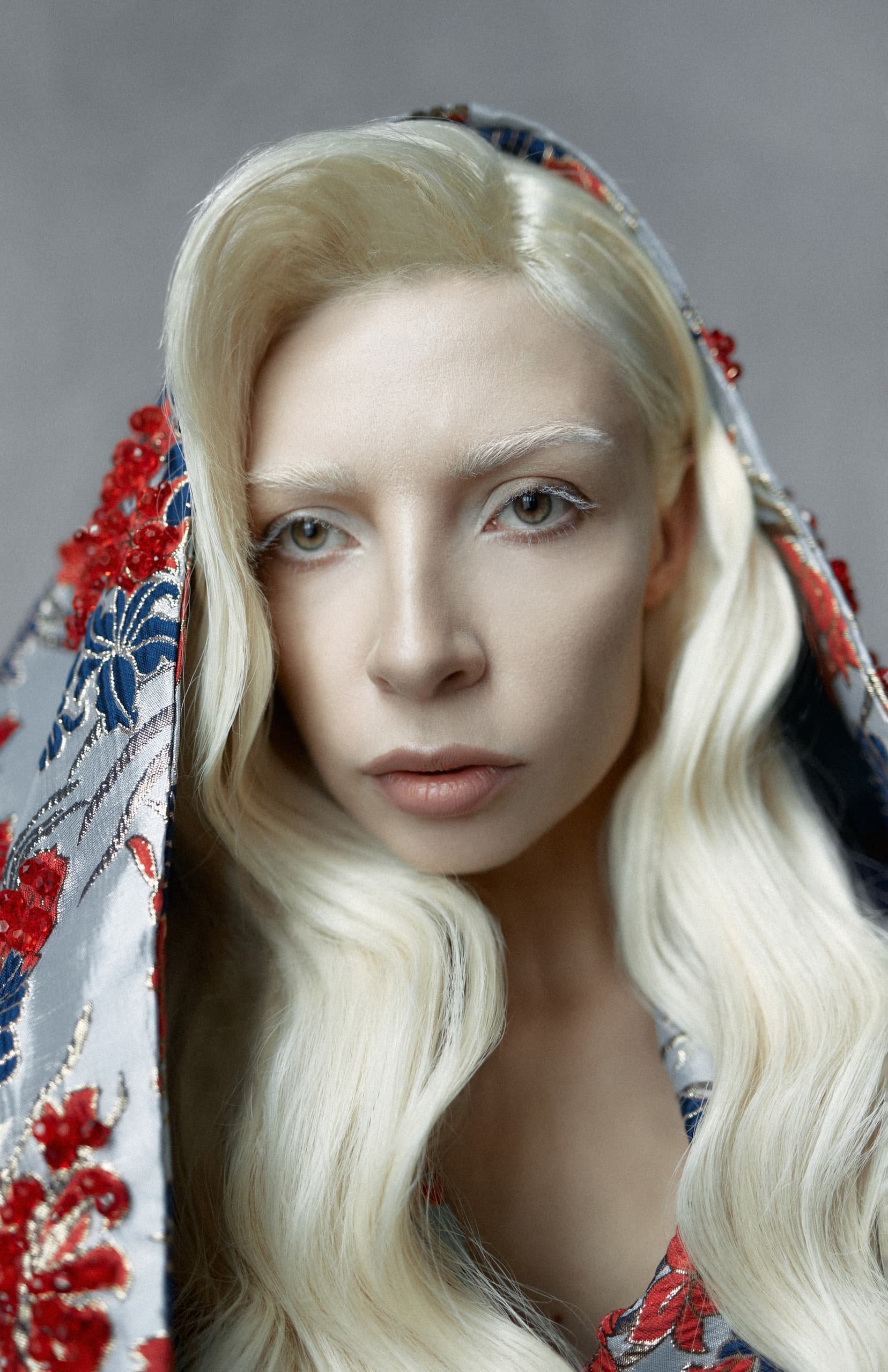Person with platinum blonde hair in a colorful floral shawl, ethereal and serene look.