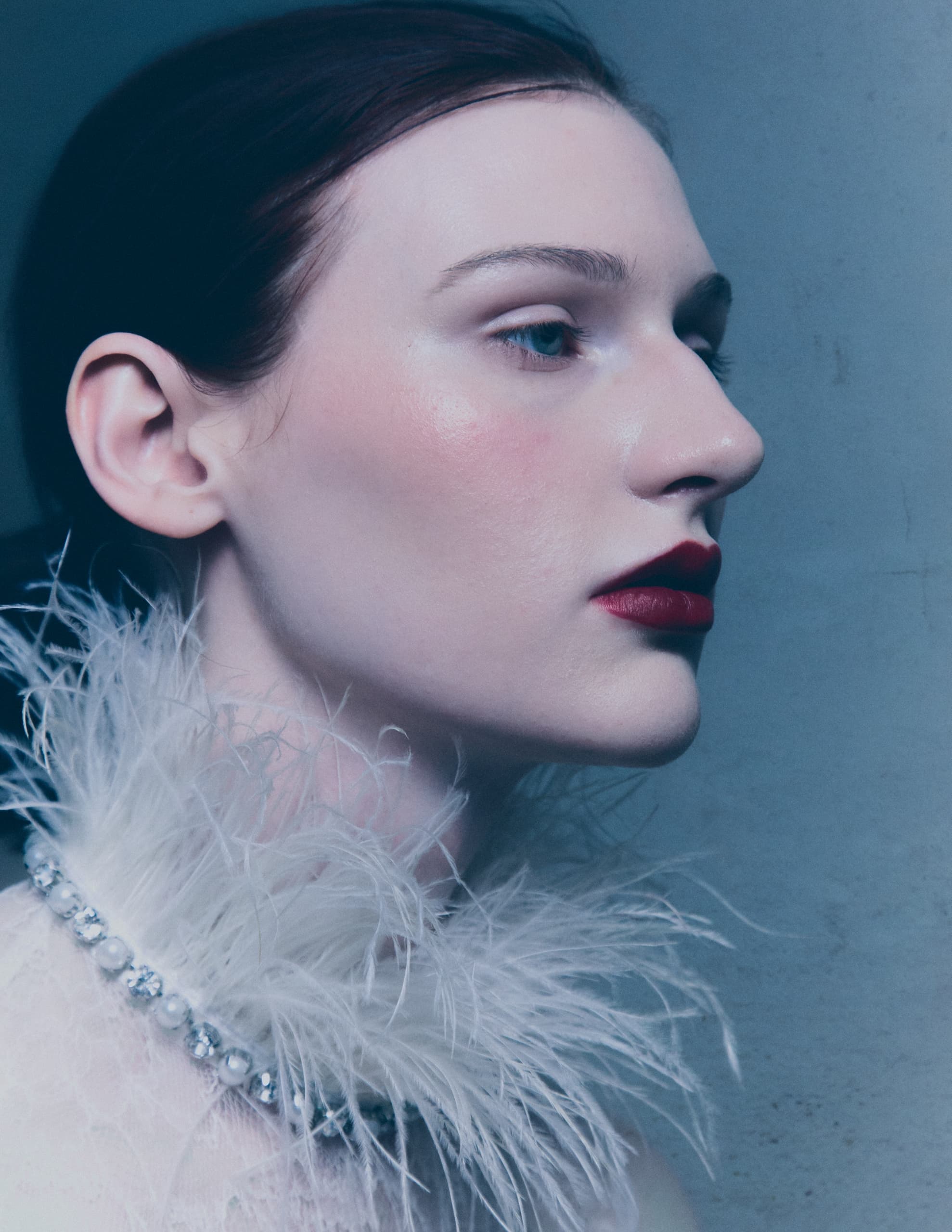 Profile of a woman with red lips and a feather collar in a dramatic pose.