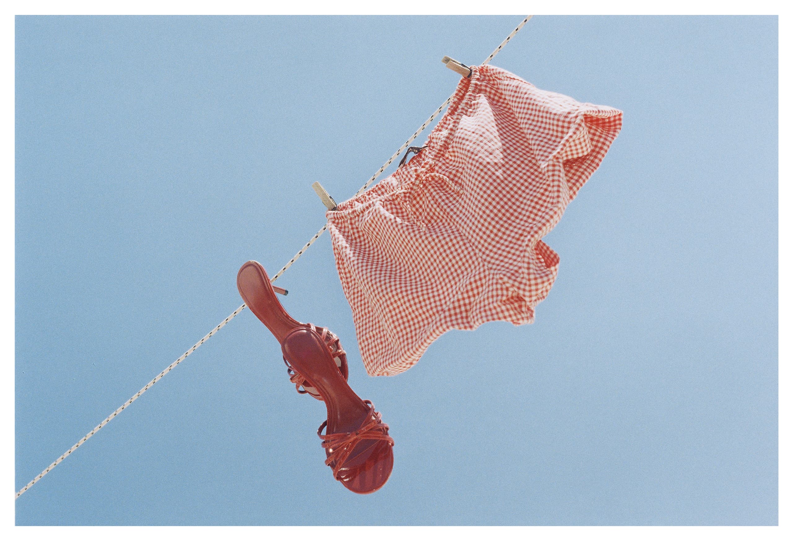 Red checkered shorts and sandals drying on a clothesline under clear blue sky.