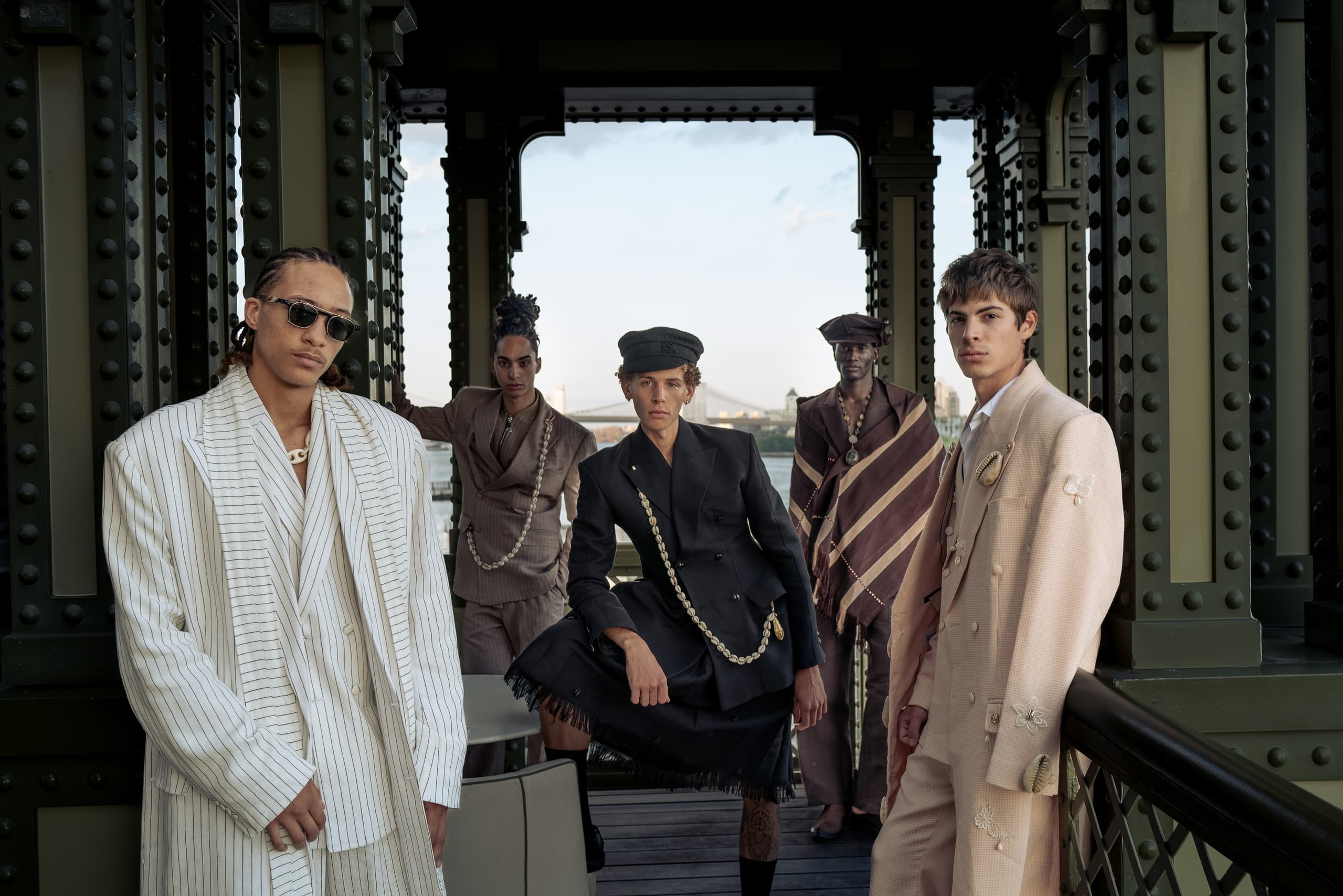 Fashionable group poses stylishly on an urban bridge, showcasing designer outfits.