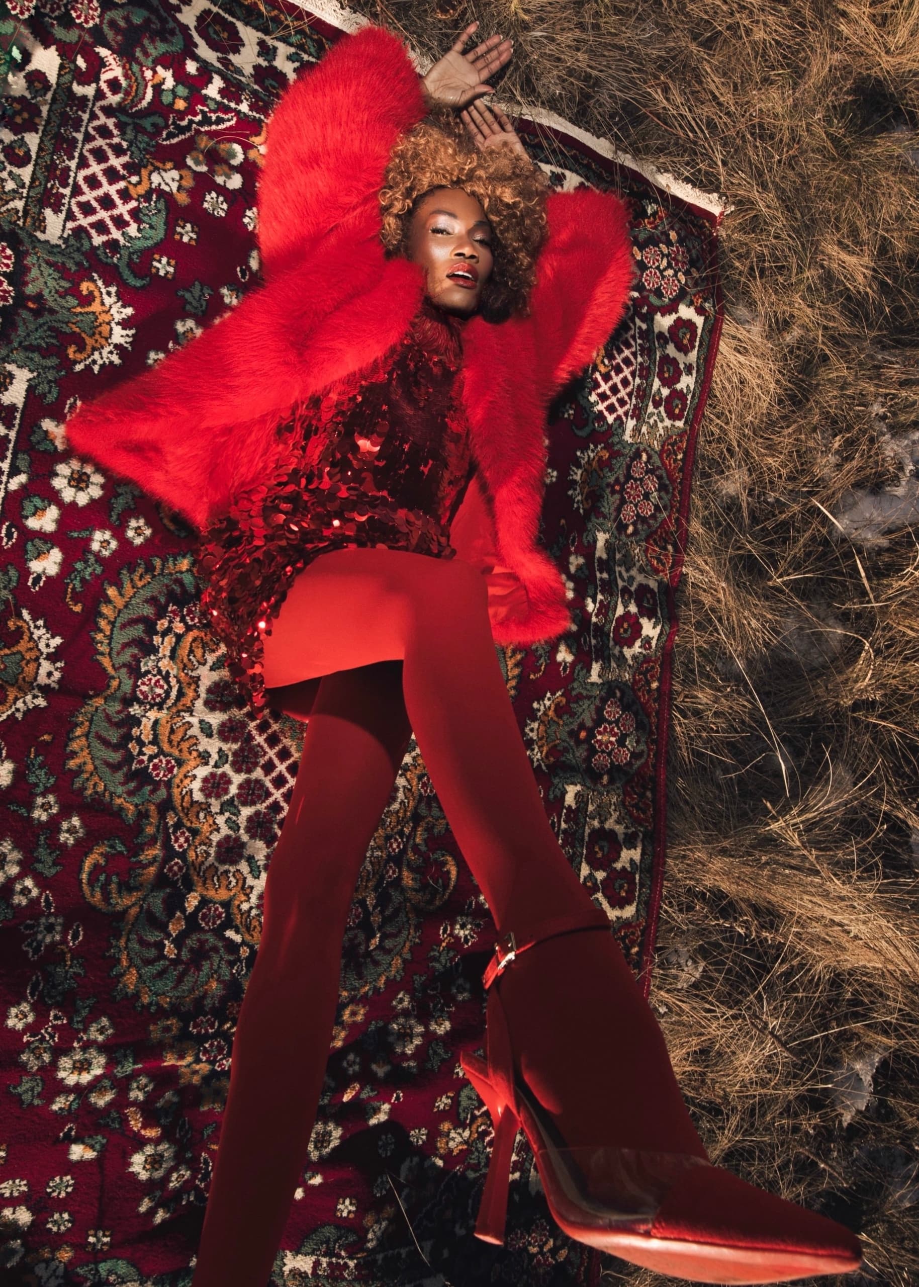 Fashionable woman in bold red attire on a patterned rug outdoors.