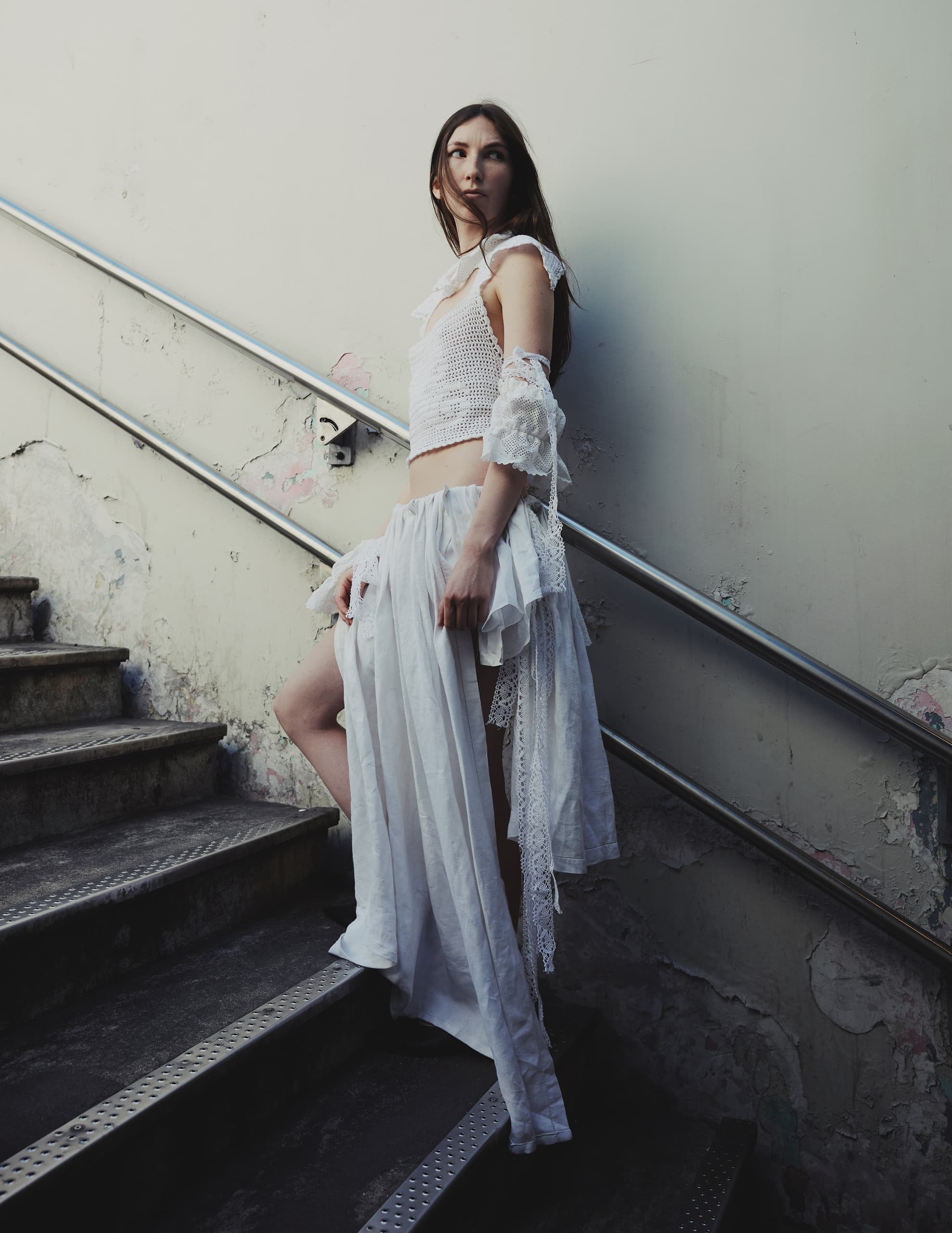 Woman in stylish white outfit posing on urban staircase.