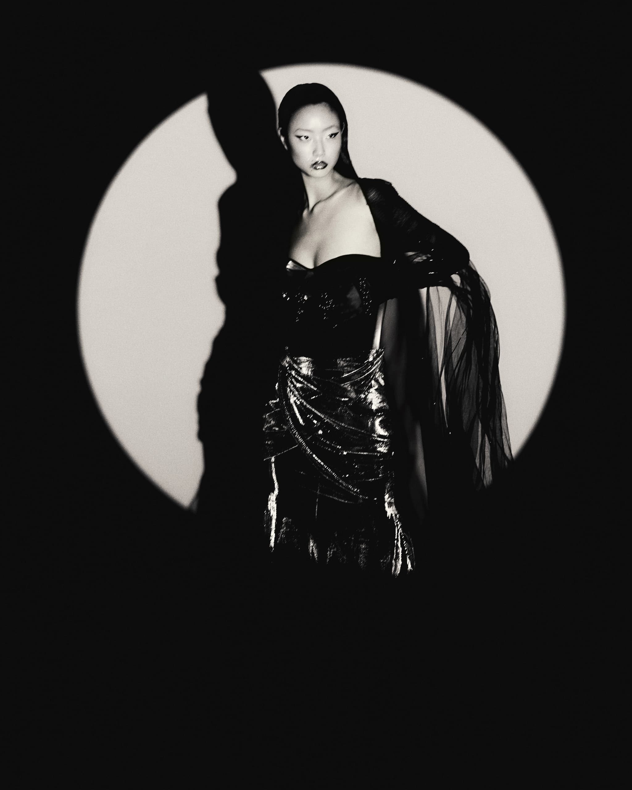 Elegant model in dramatic black attire, spotlight highlights fashion style.