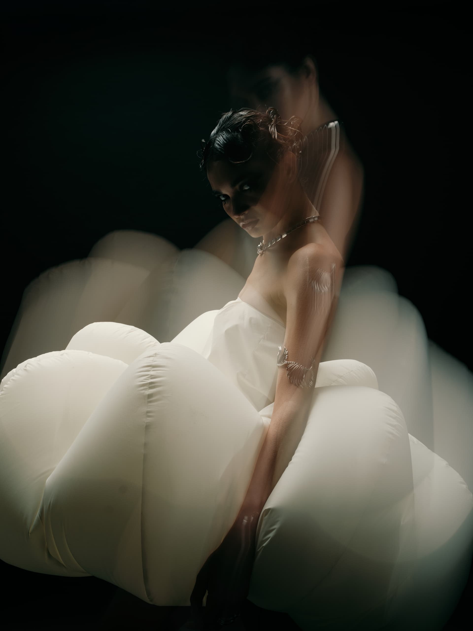 Elegant fashion model in ethereal white dress, blurred motion in dark setting