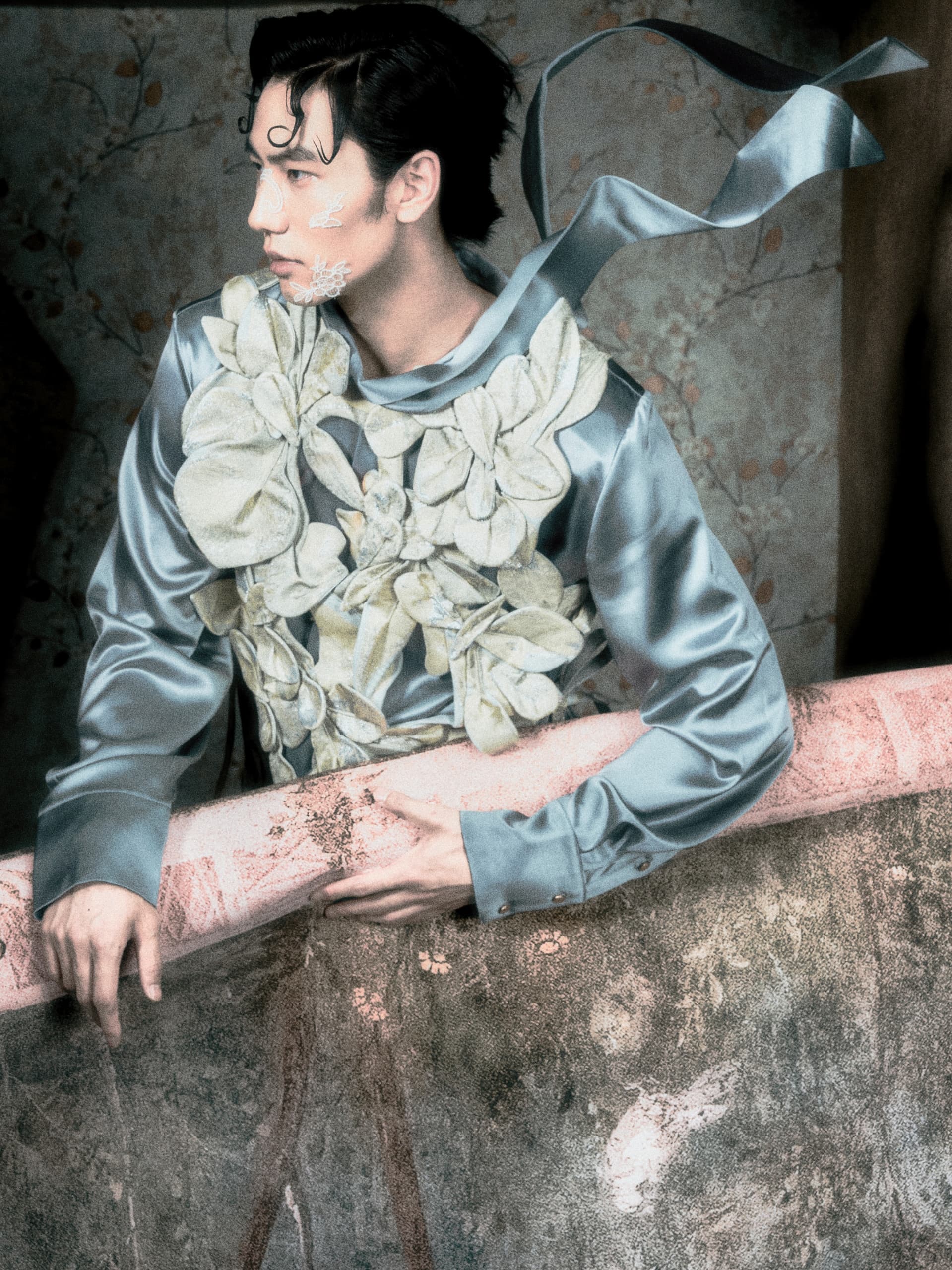 Man in floral suit leans on rustic balcony, gazing away.