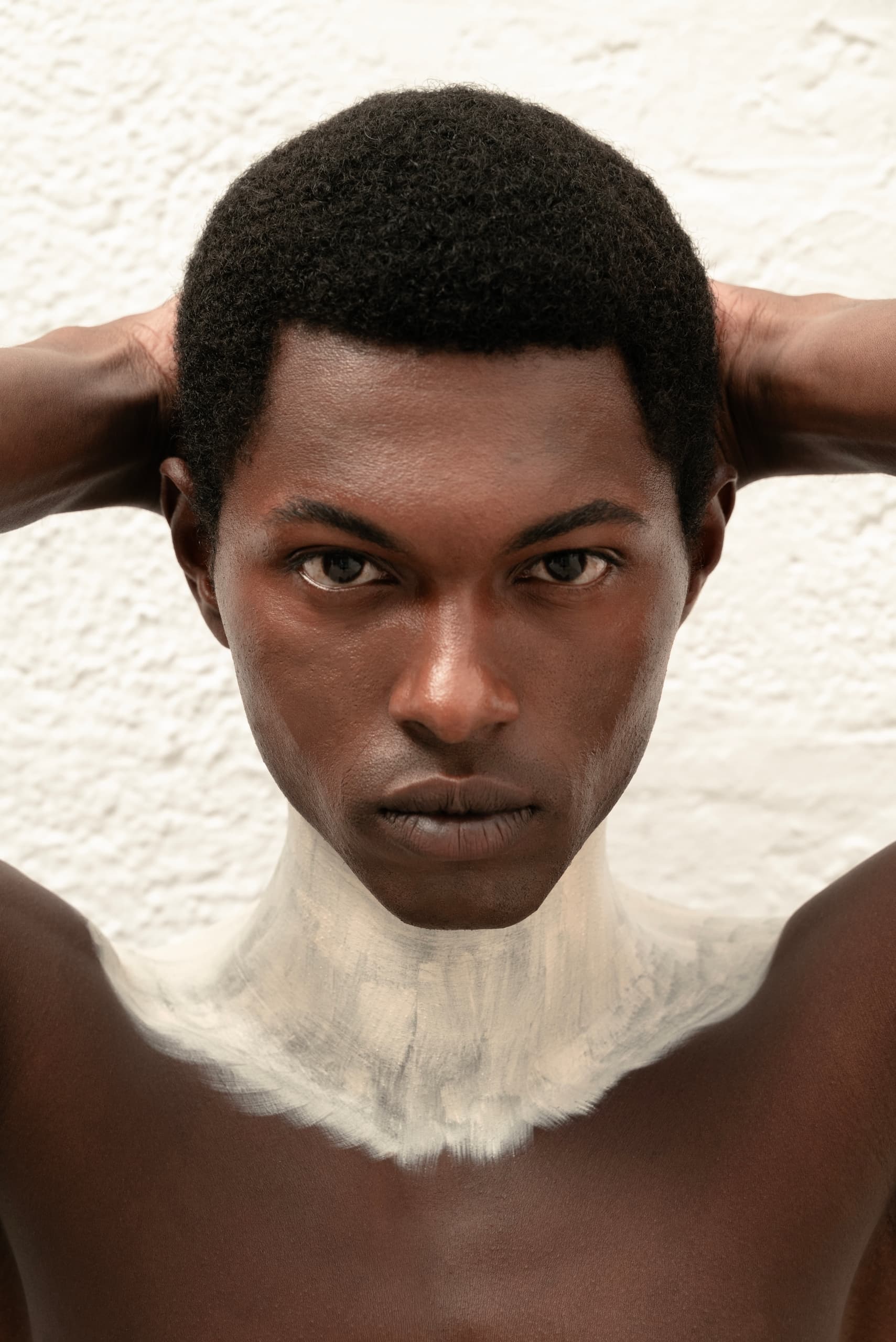Portrait of a person with artistic white paint on neck, holding hands behind head.