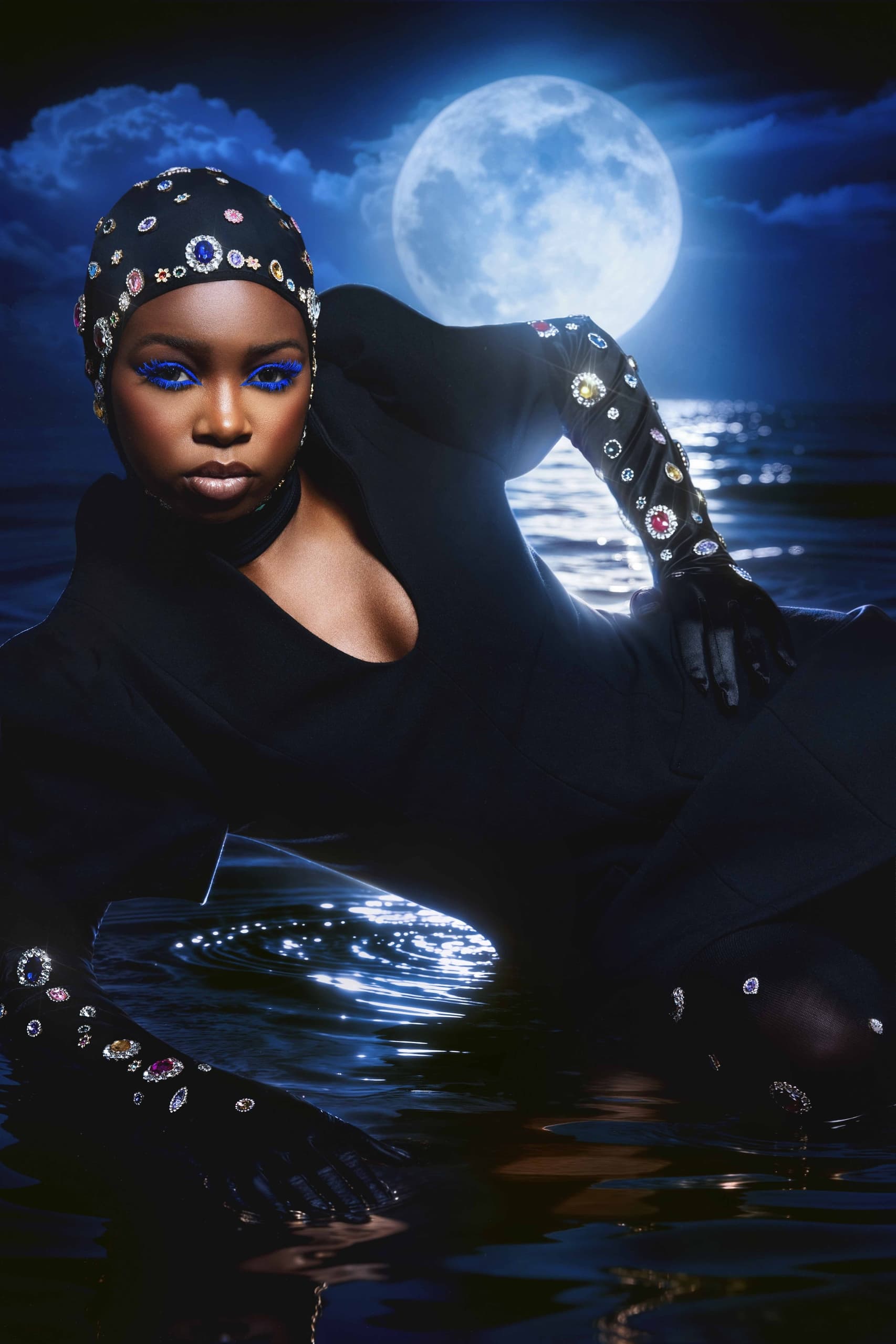 Fashion model poses under full moon with jeweled attire and vibrant blue makeup.