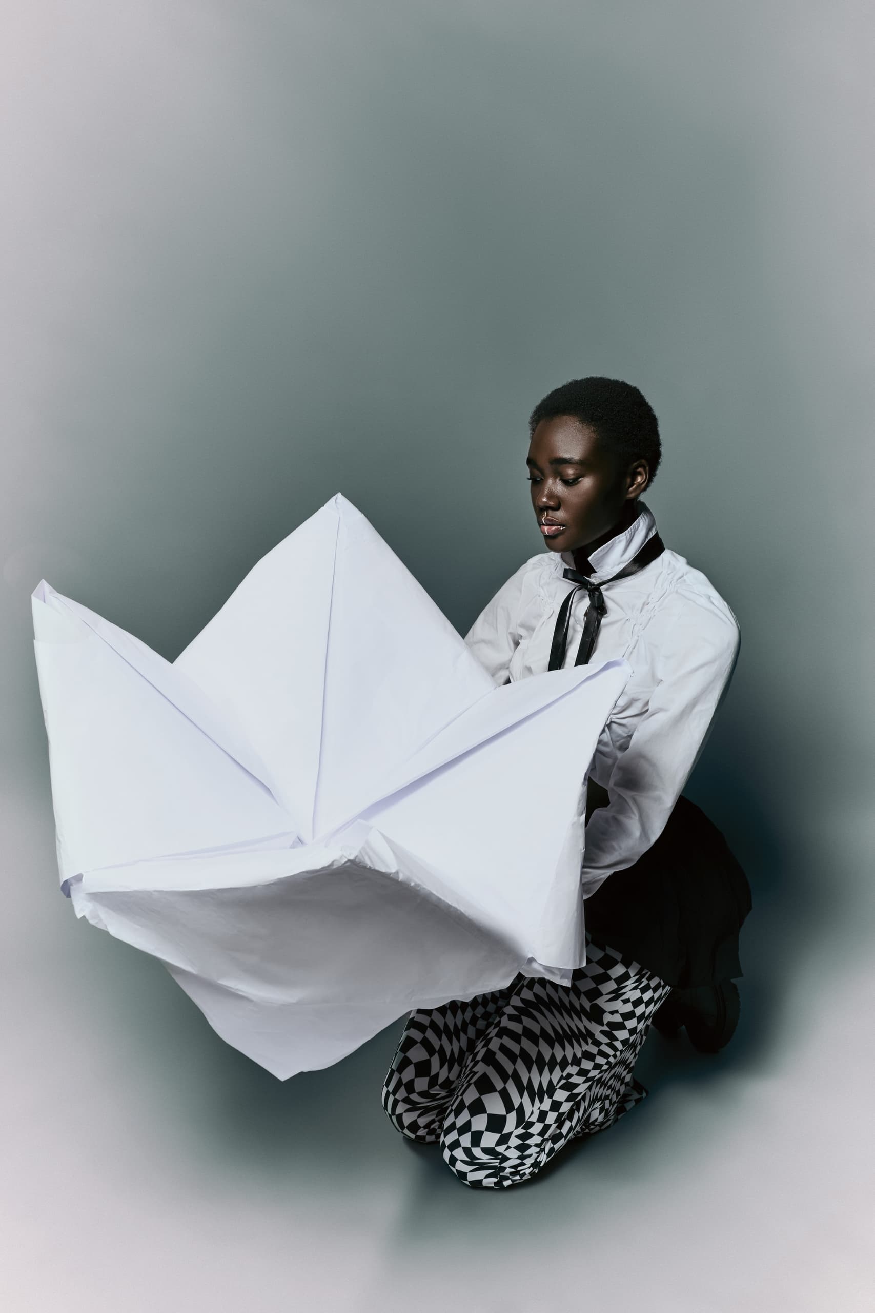 Person in black and white outfits holding a large folded paper shape.