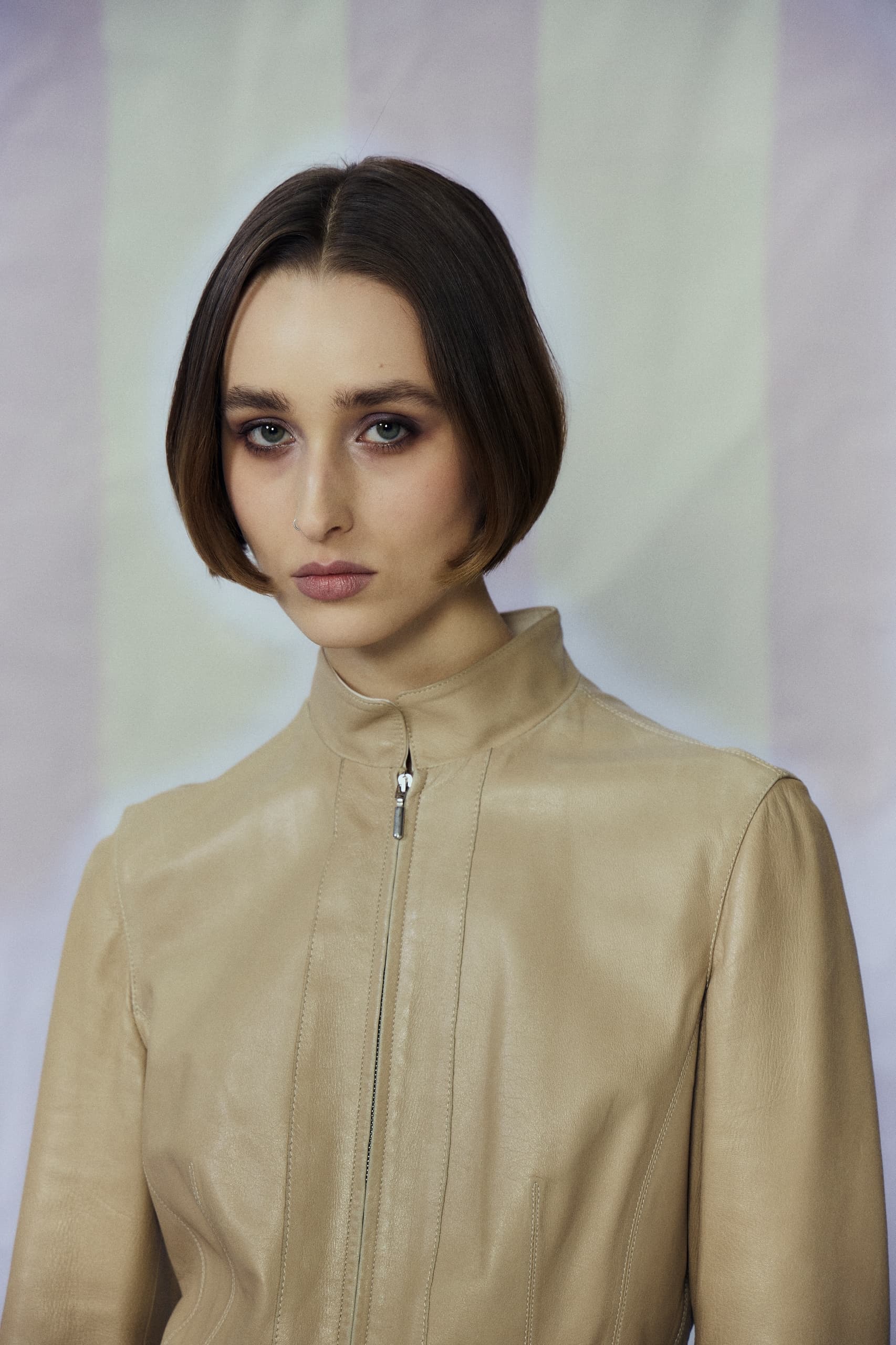 Woman in beige leather jacket with short bob haircut against soft background.