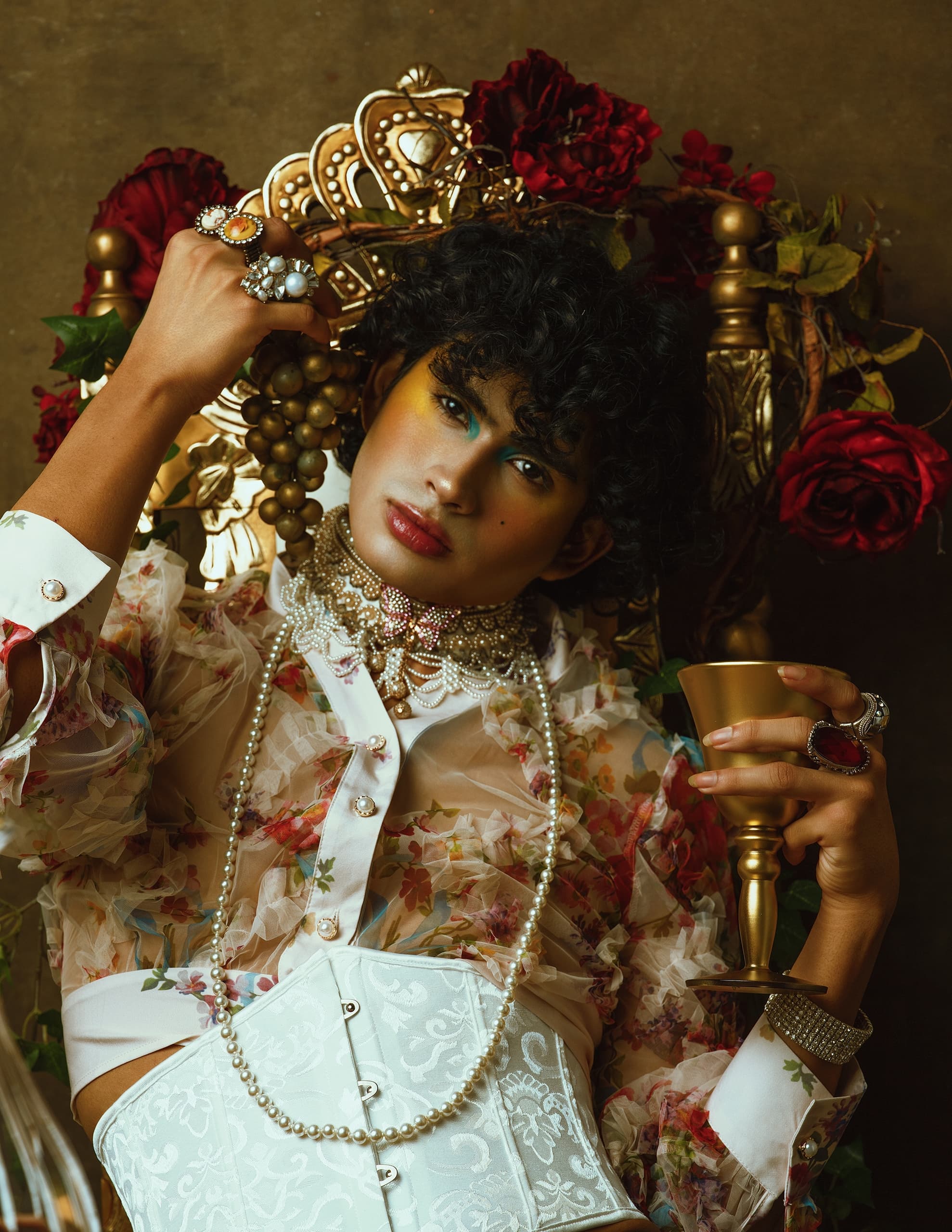 Fashionable person in ornate attire with gold goblet and jewelry, surrounded by roses.