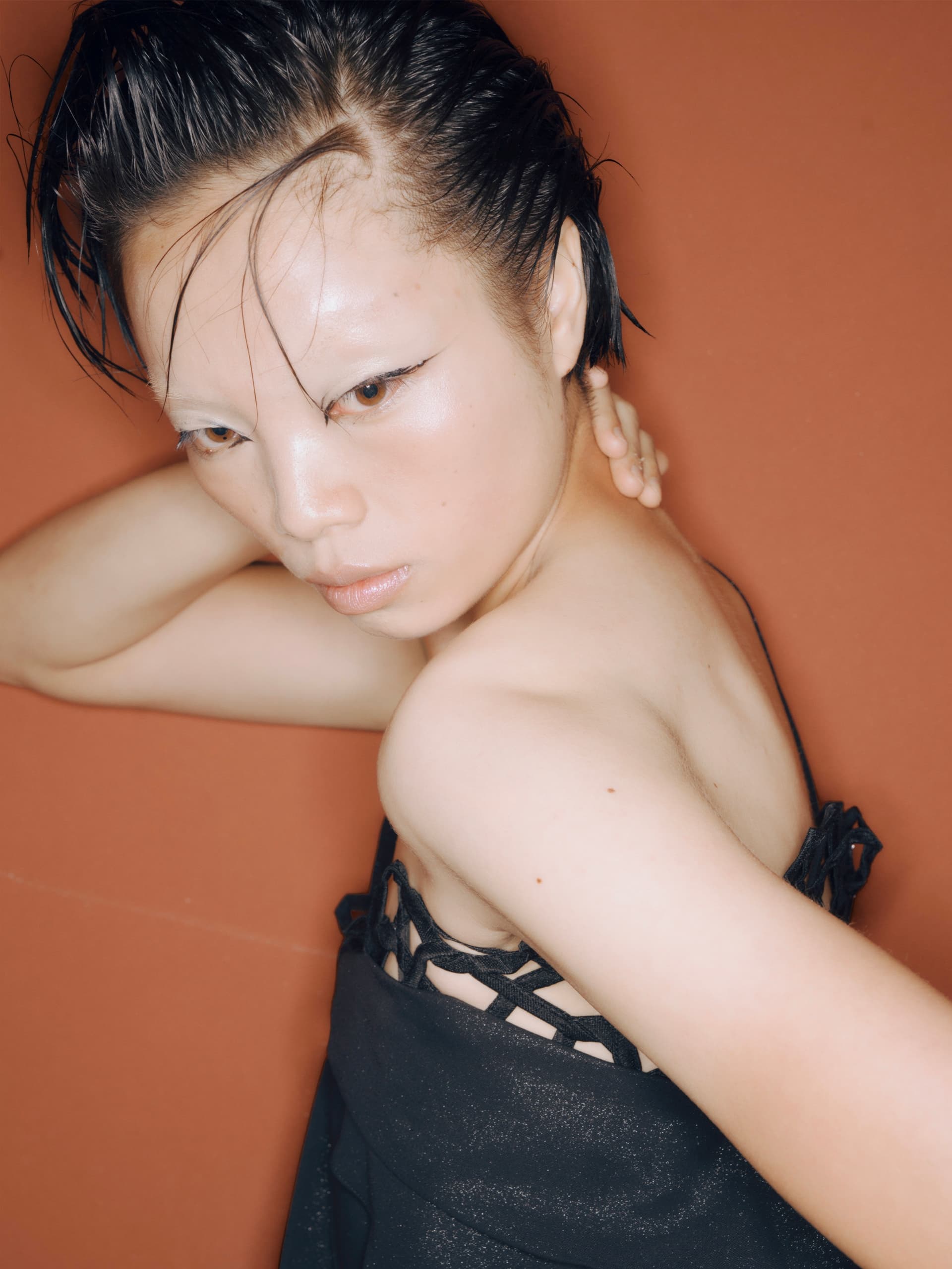 Model with striking makeup and short hair against an orange background.