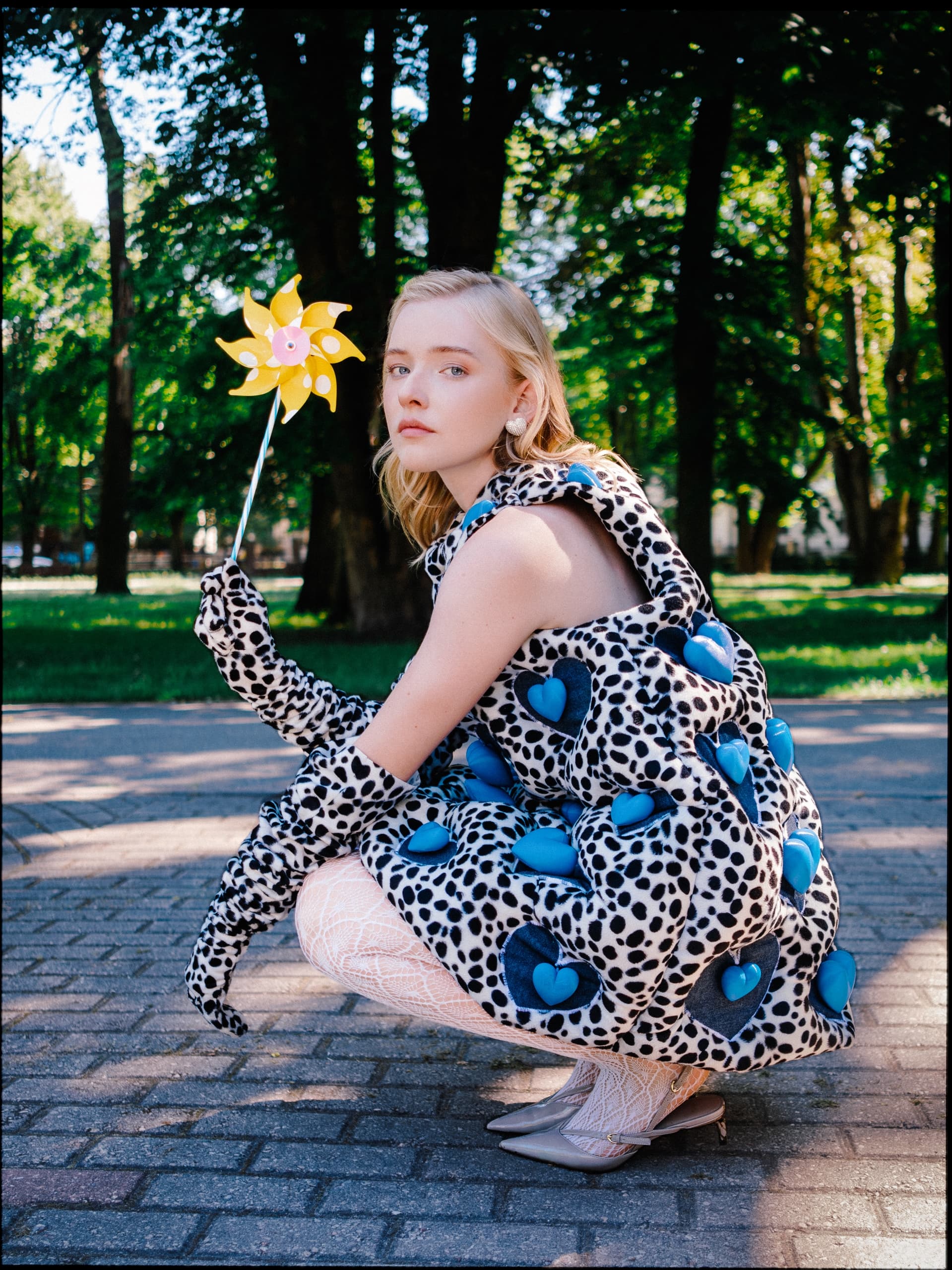 Fashionable woman in polka-dot outfit holding pinwheel in sunny park.