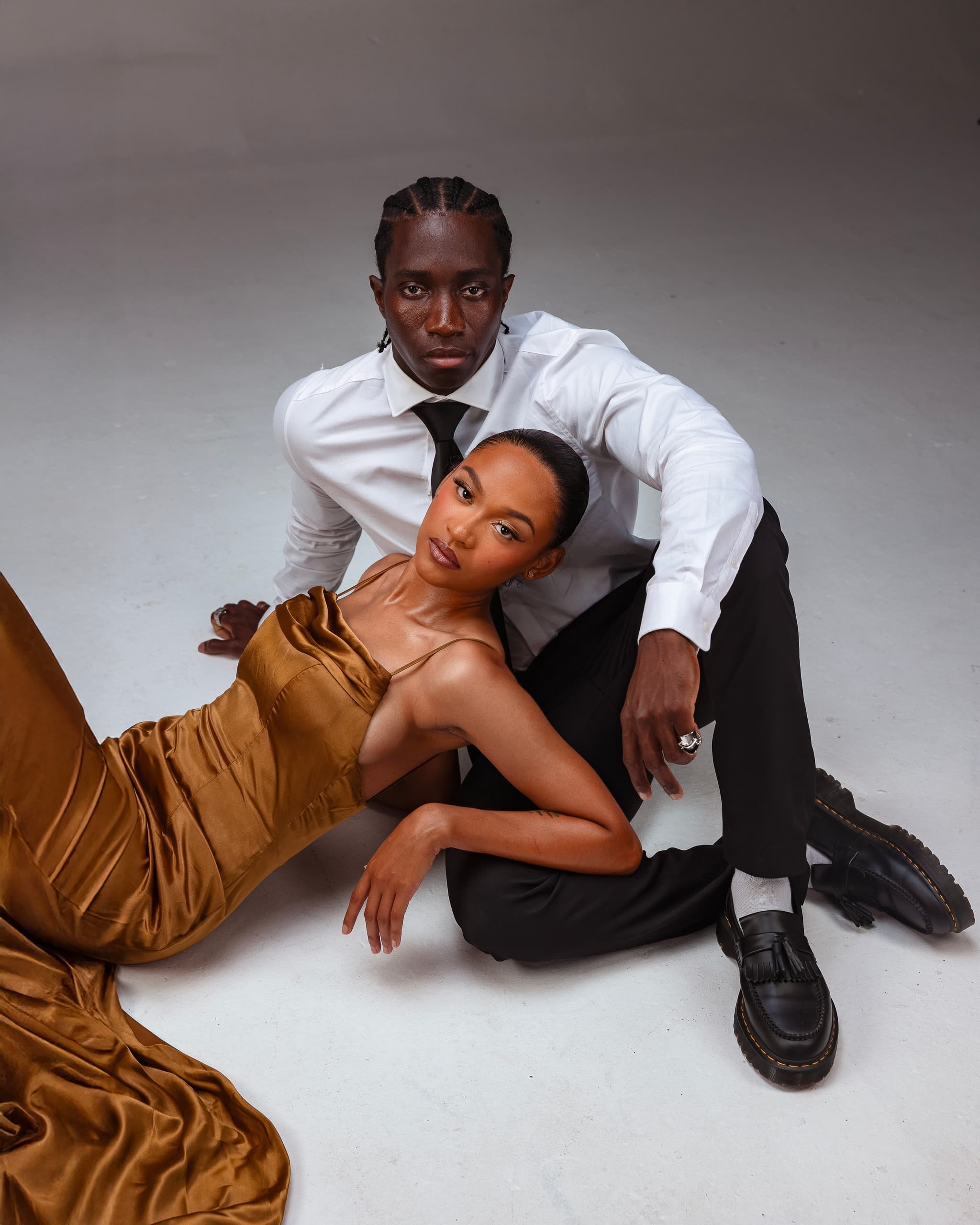 Elegant couple in formal attire posing on a studio floor.