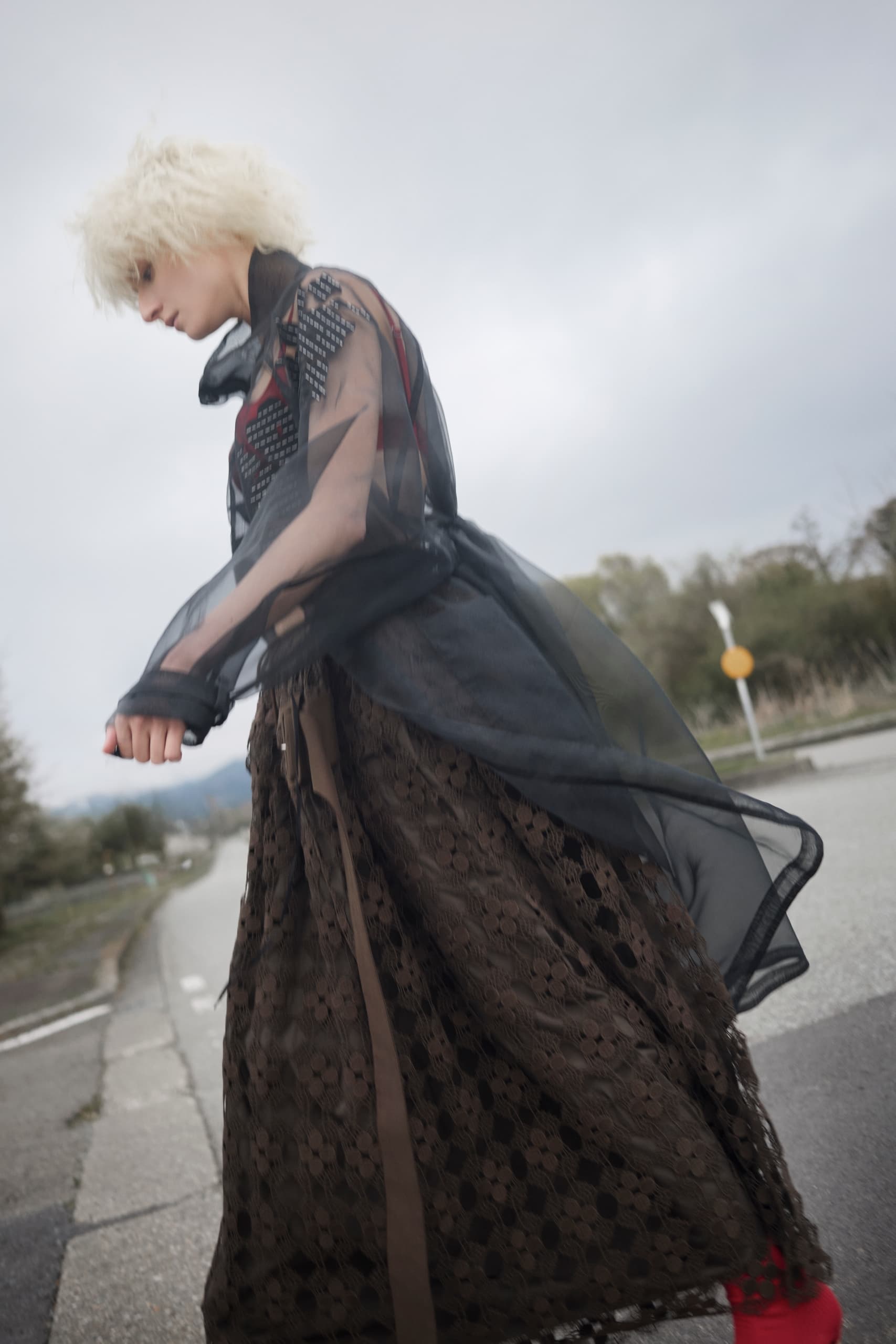 Fashionable person in a flowing lace outfit walking outdoors on a cloudy day.
