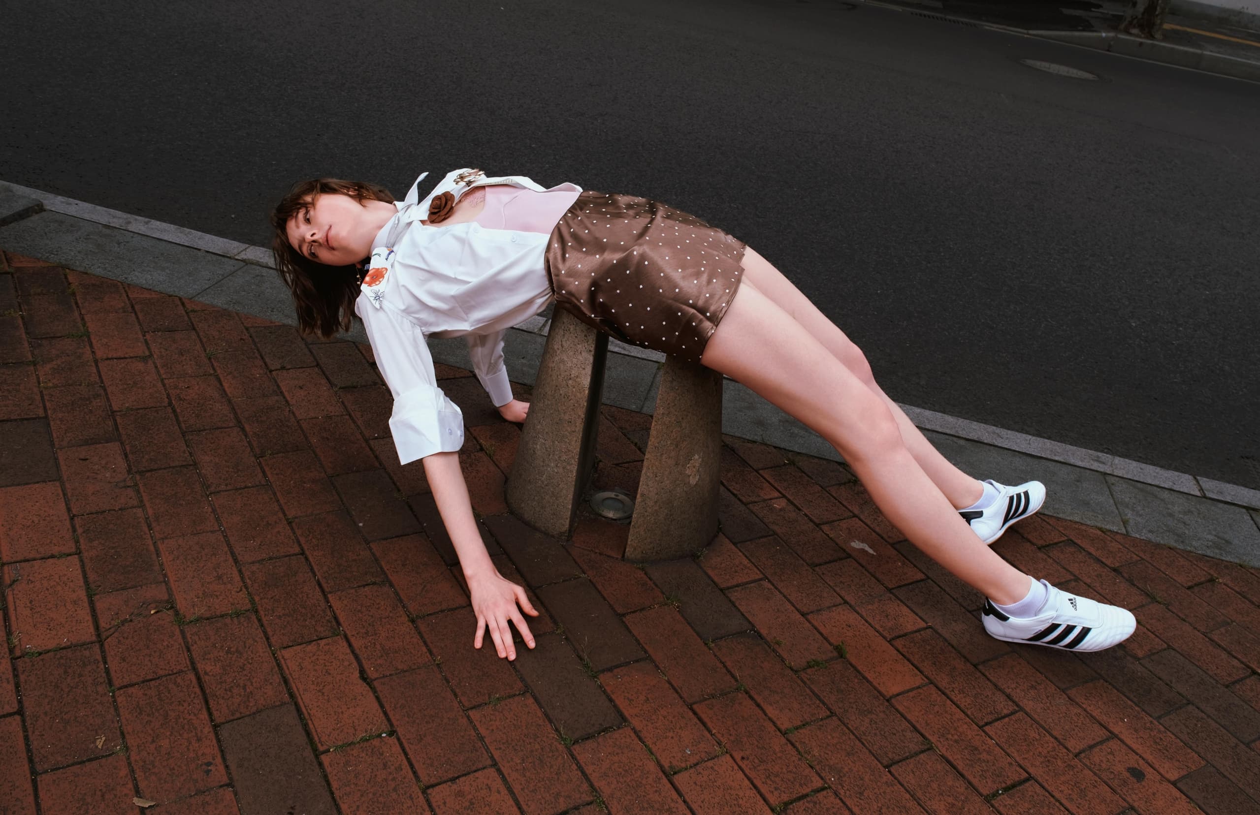 Person balancing creatively on urban pavement in stylish fashion outfit and sneakers.