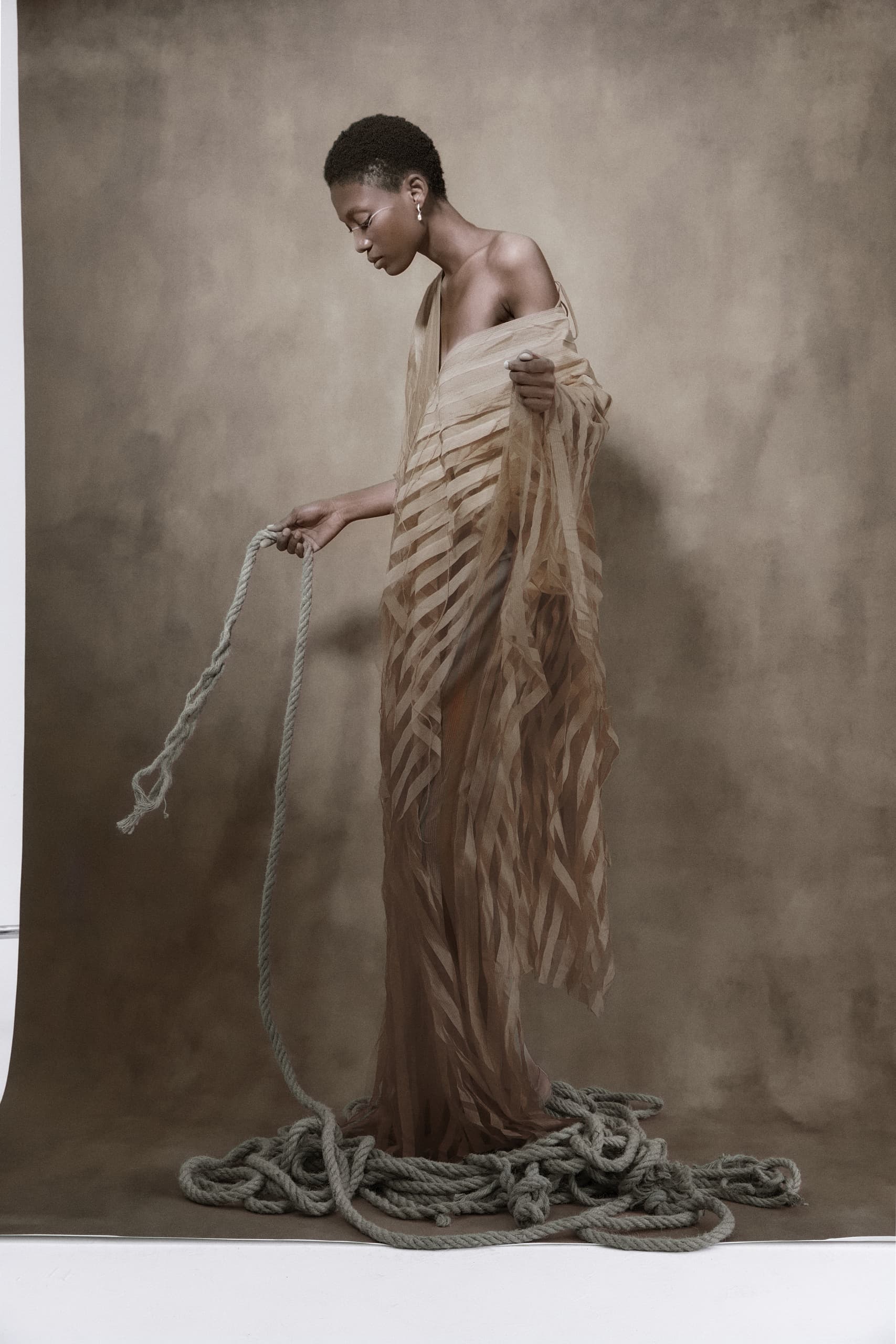 Elegant figure with draped fabric, holding a rope on a textured backdrop.