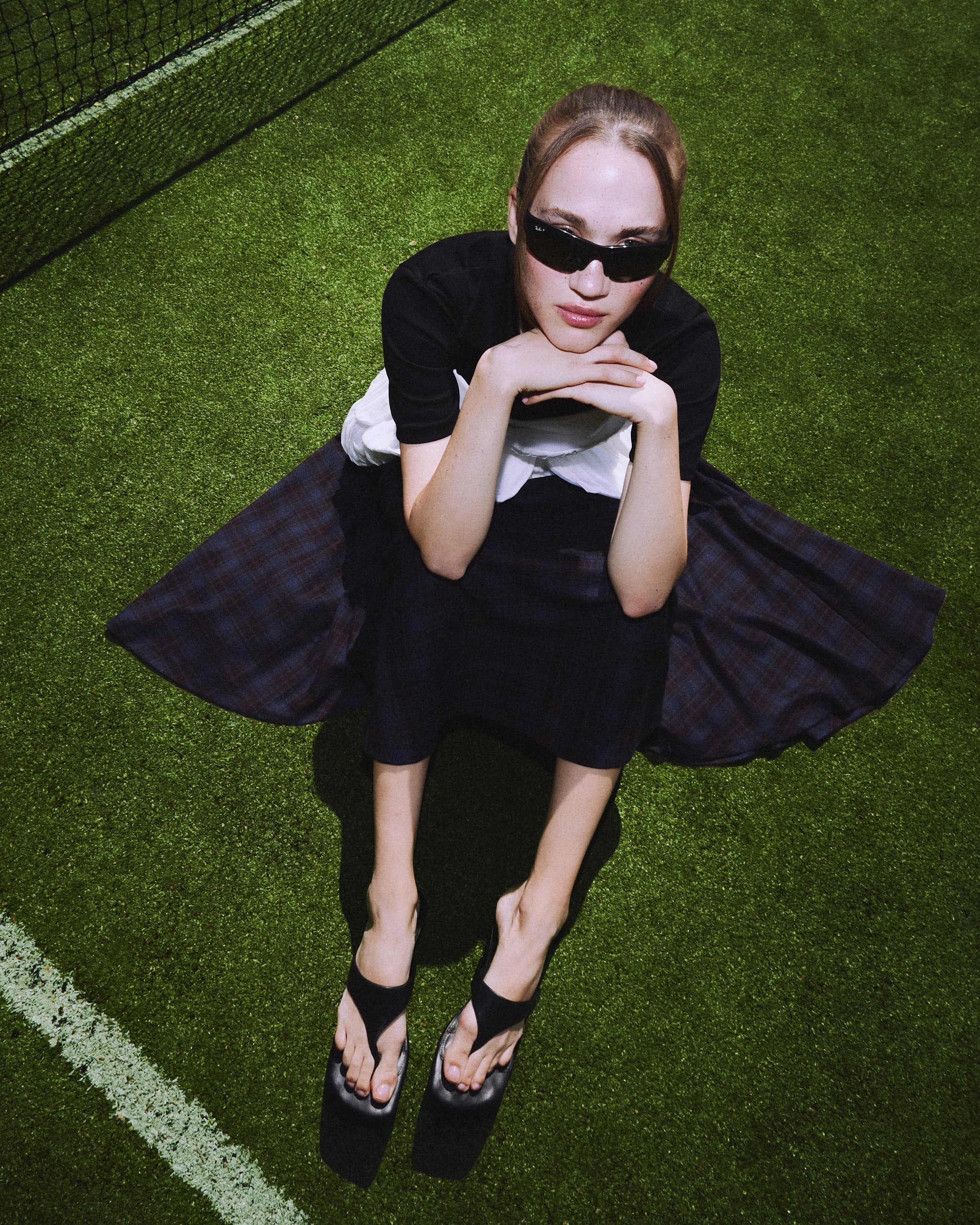 Fashionable woman in sunglasses and sandals sitting on grass.
