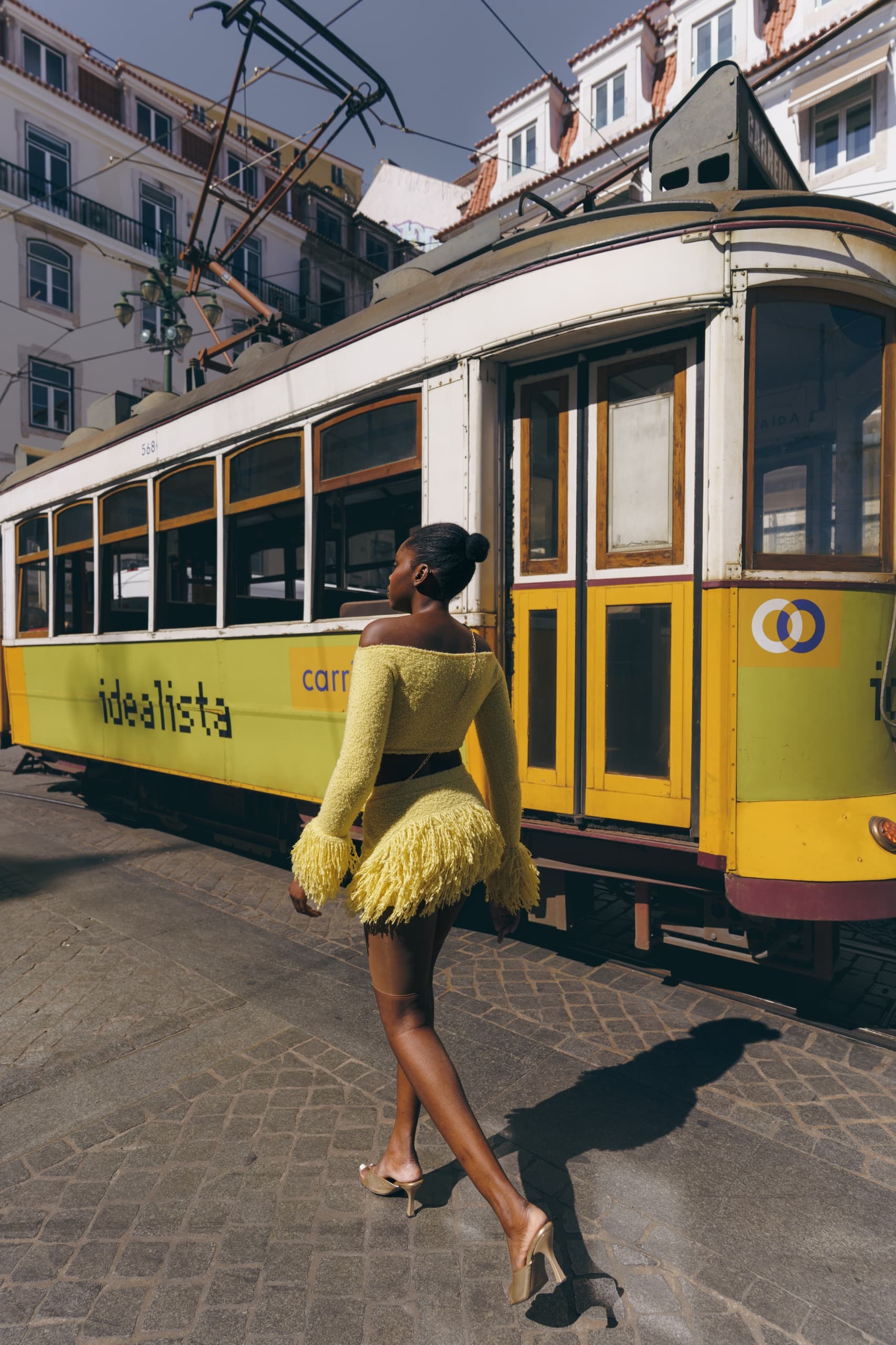 Woman in yellow dress walking past vintage streetcar in Lisbon.