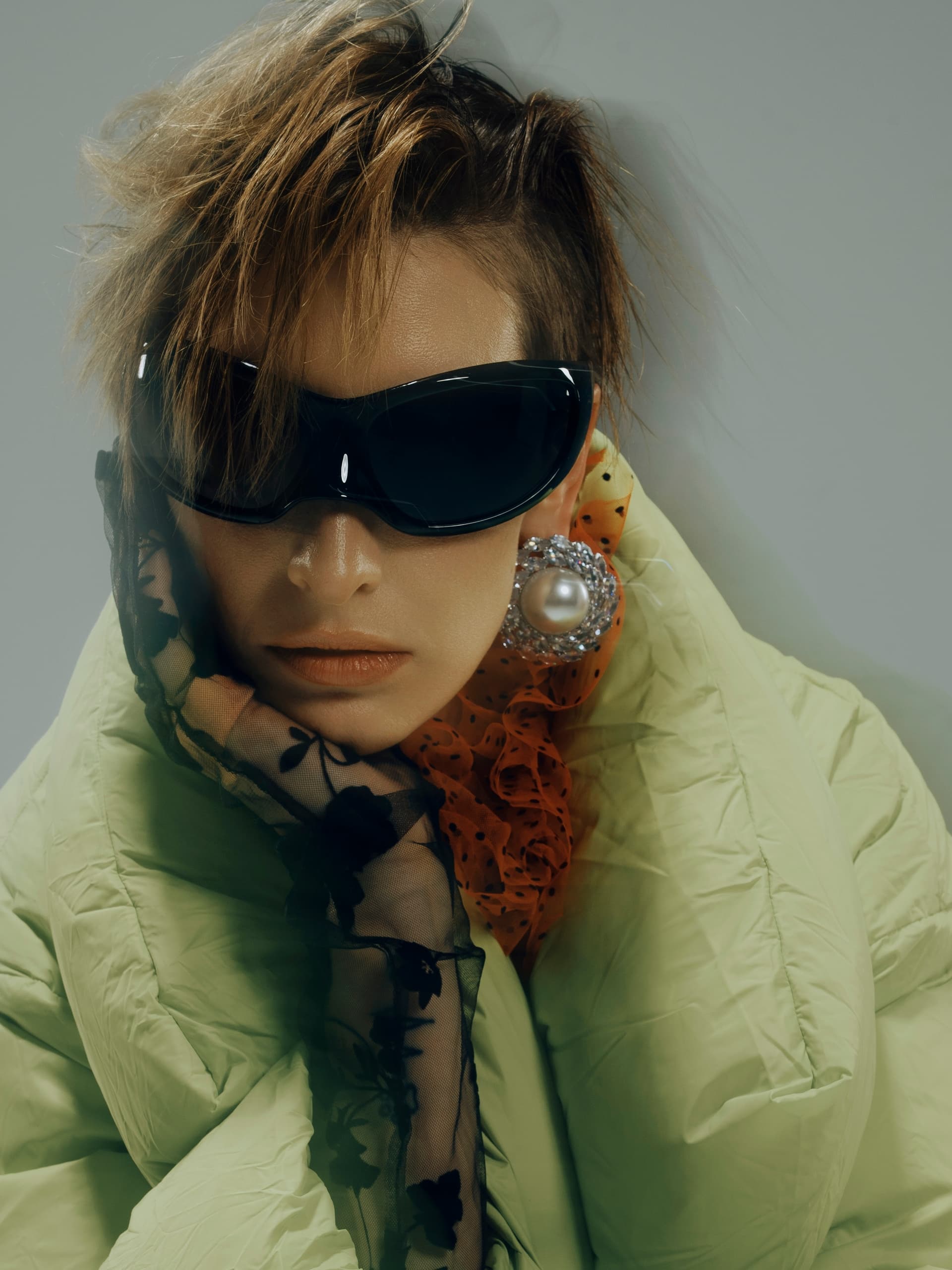 Chic woman in oversized sunglasses and green puffer jacket, stylish winter fashion.