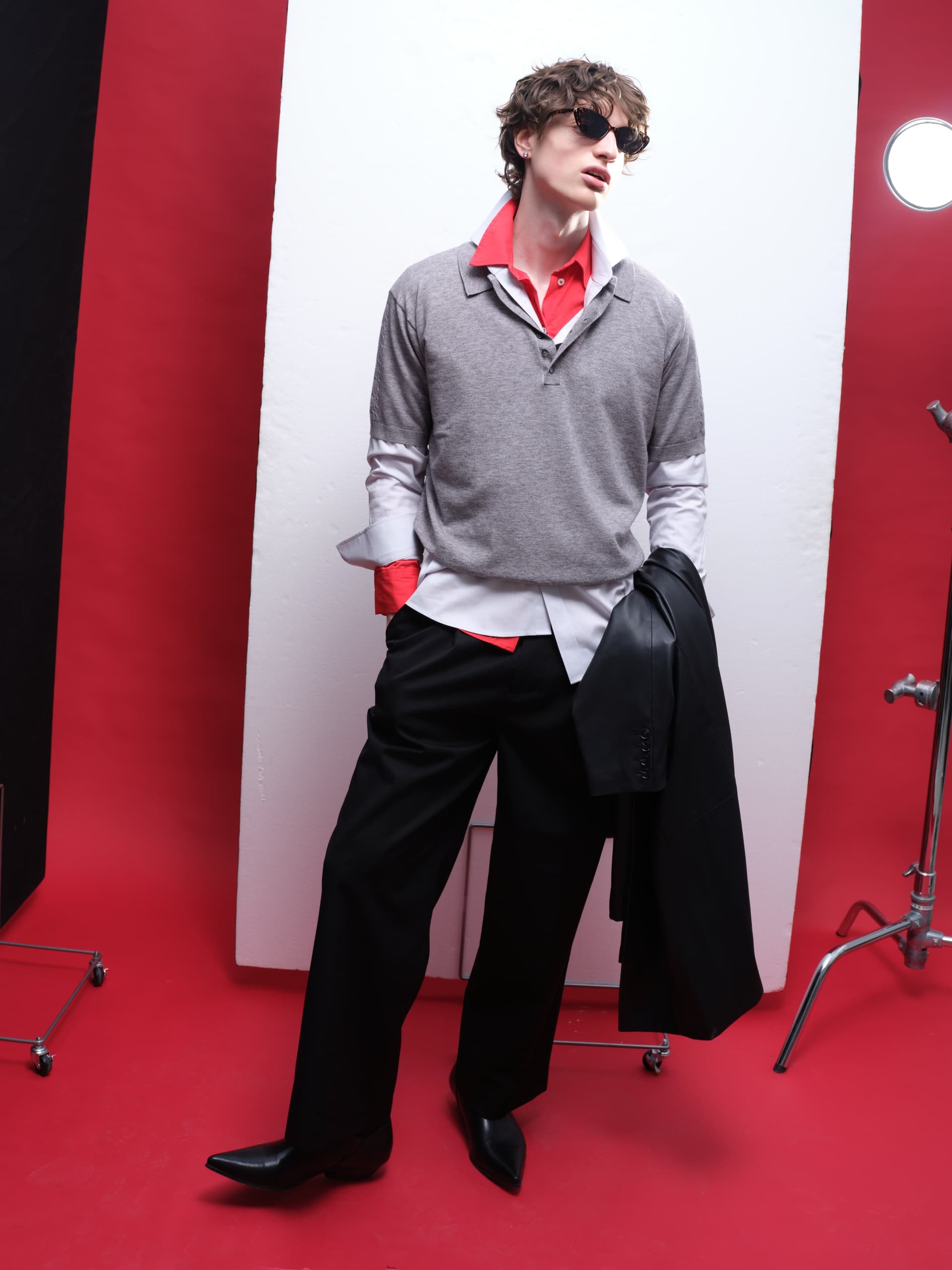 Trendy fashion model in layered outfit with sunglasses on a red background.