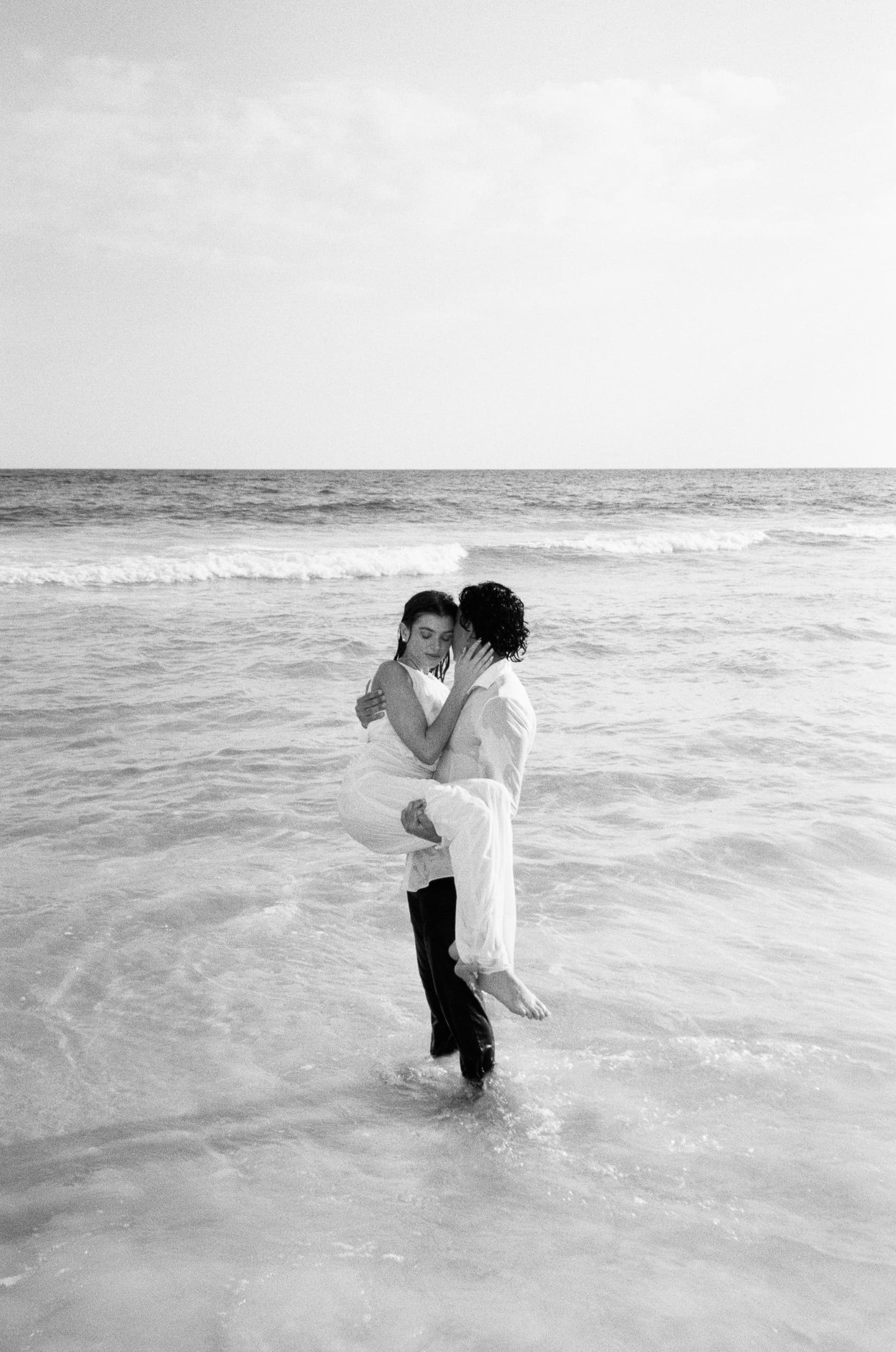 Romantic couple embracing in ocean waves on a sunny day.