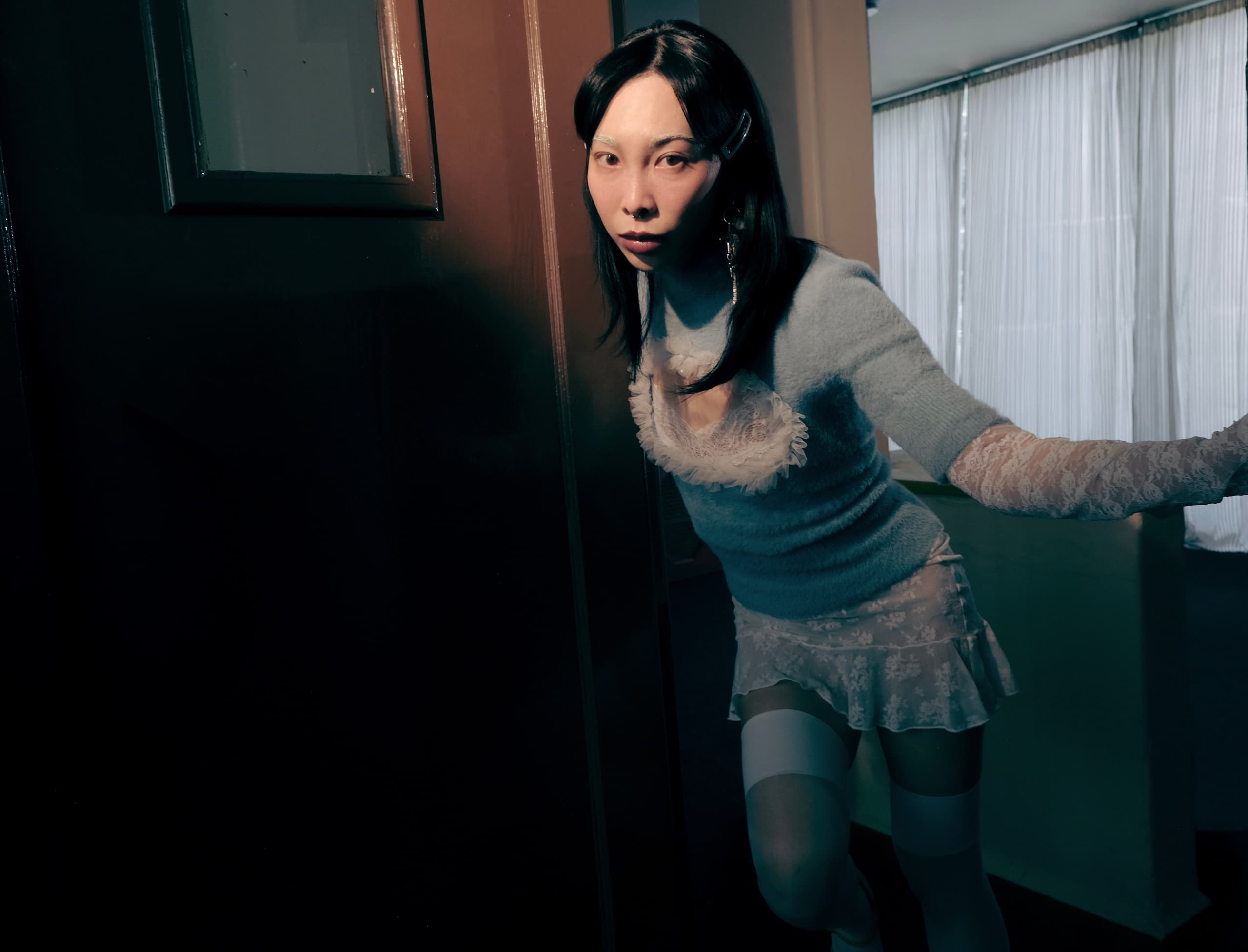 Person in chic outfit leans on door in moody lighting.