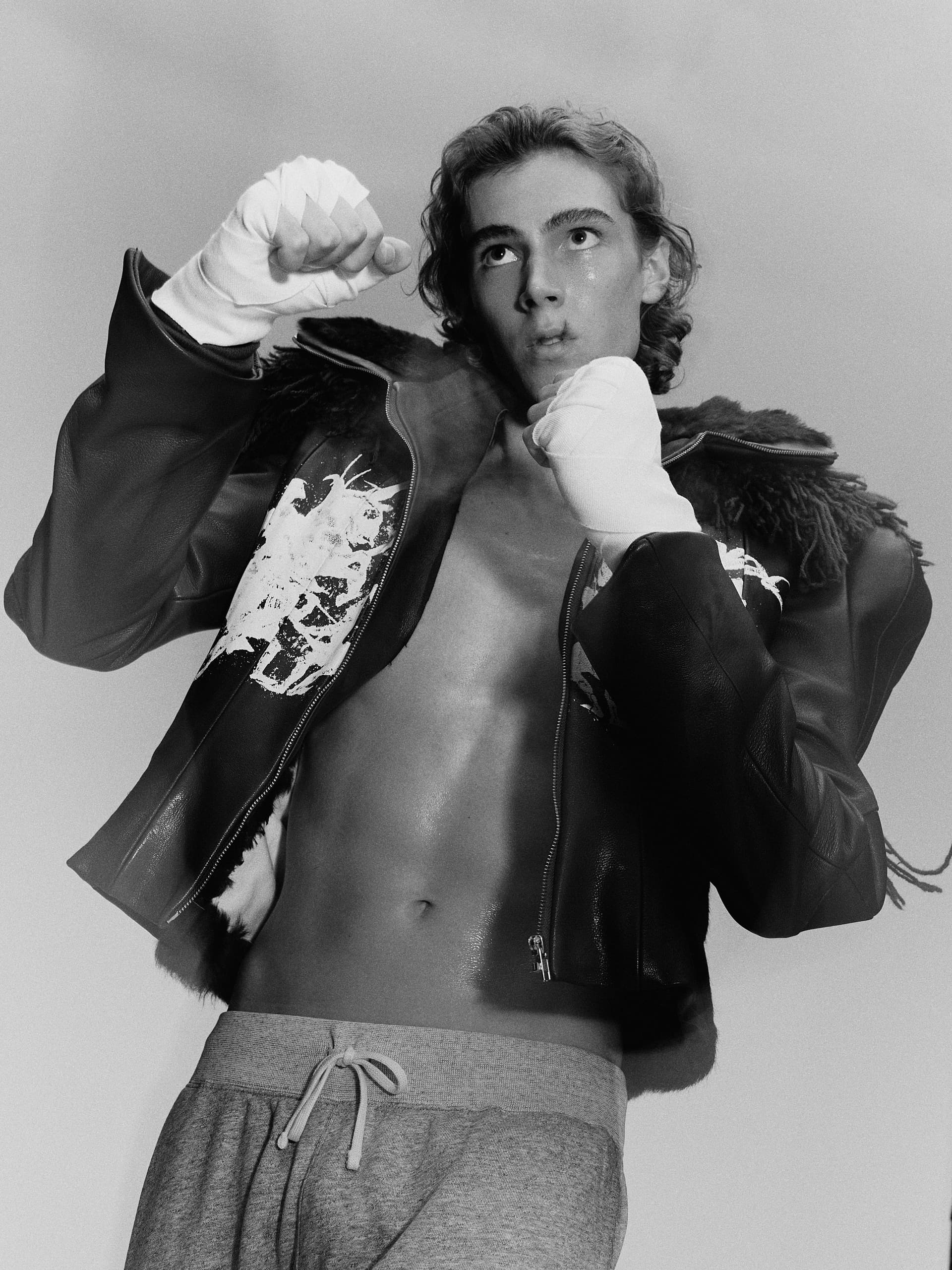 Person posing in boxing stance, wearing leather jacket and hand wraps.