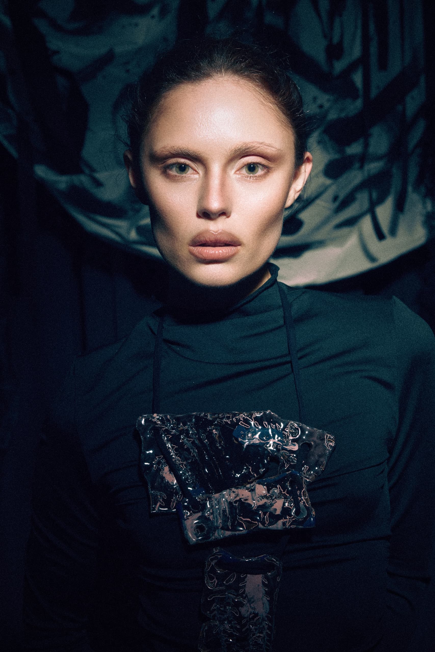 Model in dark fashion outfit with metallic accents, moody artistic backdrop.