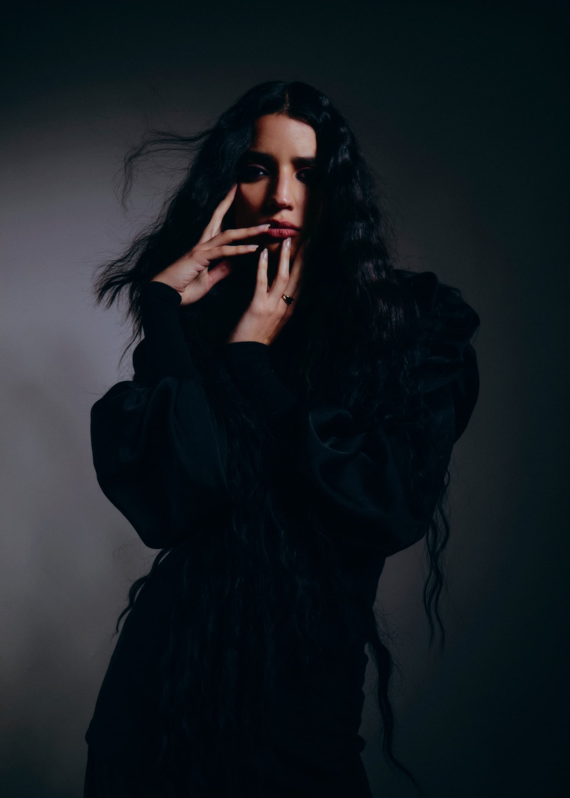 Woman in dramatic pose with long, flowing hair wearing a dark, puffy-sleeved dress.