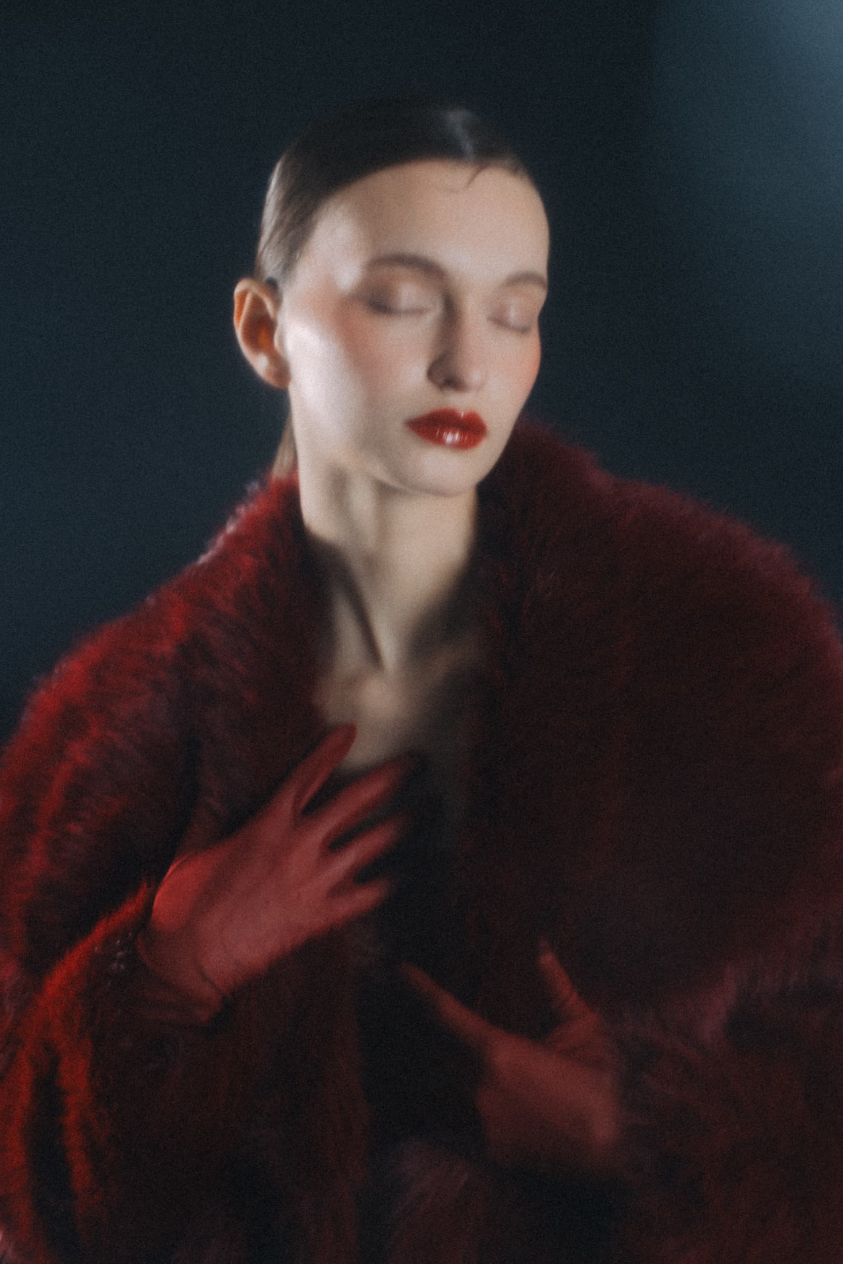 Elegant woman in red fur coat and gloves with closed eyes.