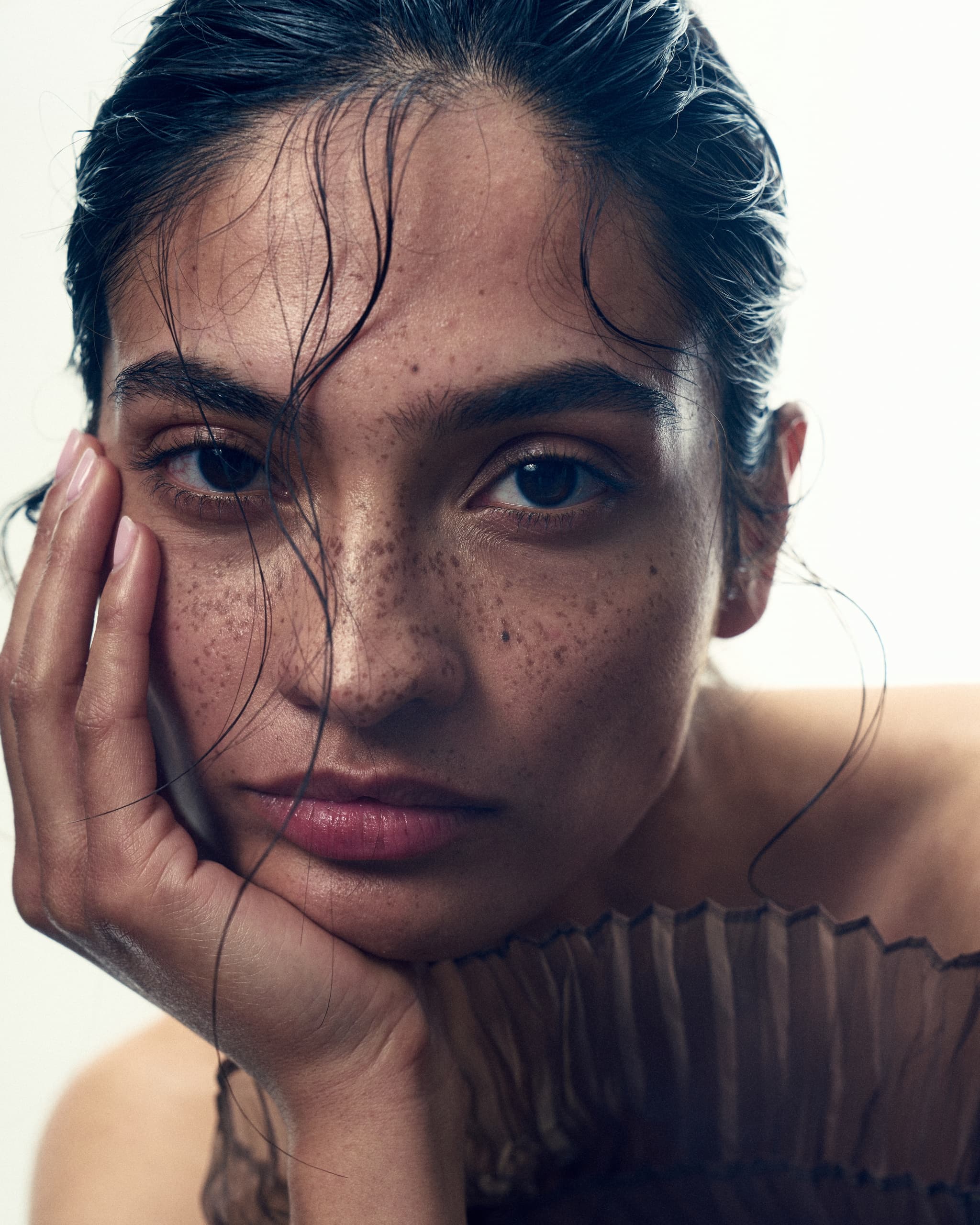 Portrait of a contemplative person with freckles and hand on face, artistic lighting.