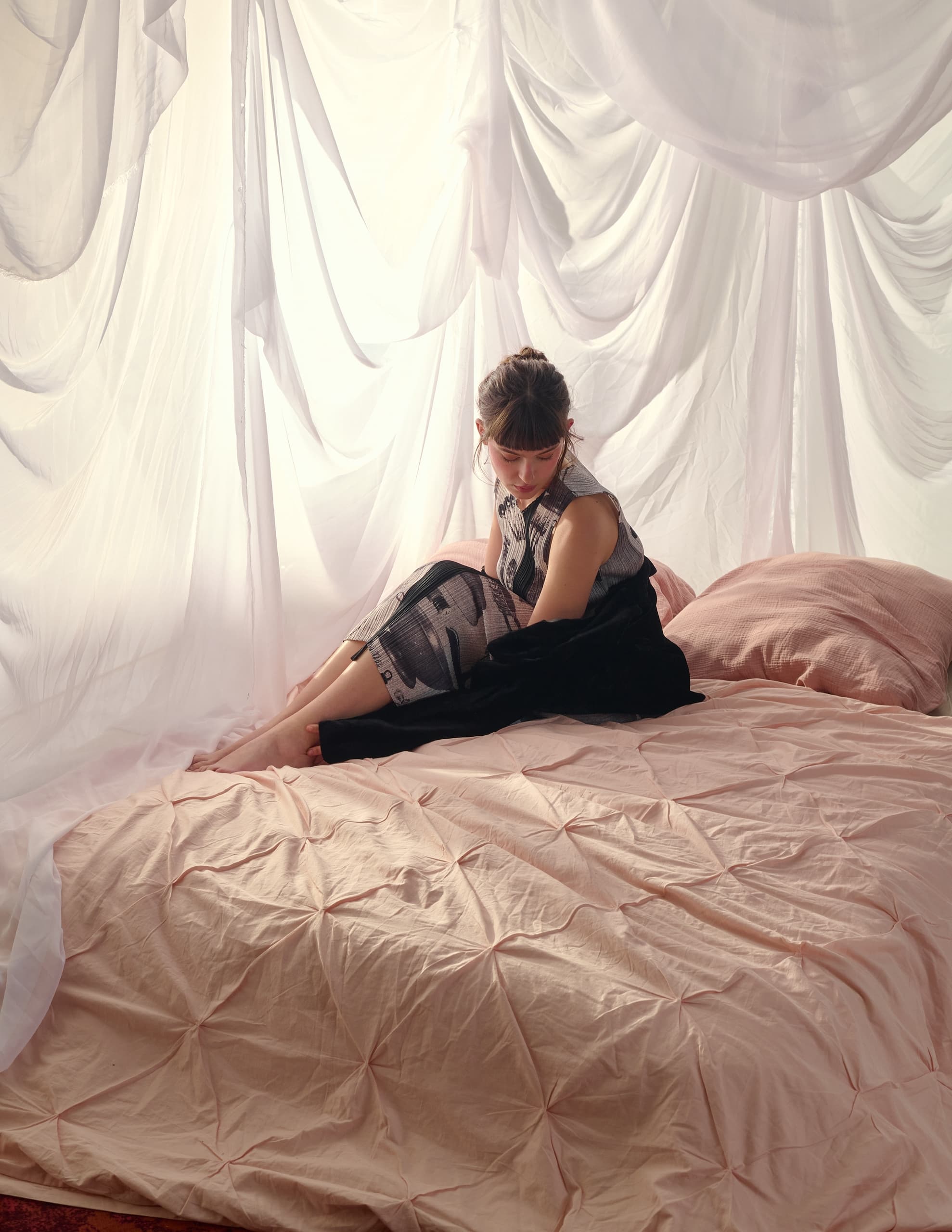Cozy bedroom scene with soft pink bedding and draped white curtains.