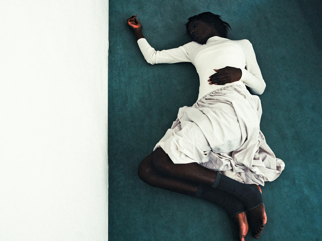 Person in white top and skirt lying on green surface, peaceful and relaxed pose.