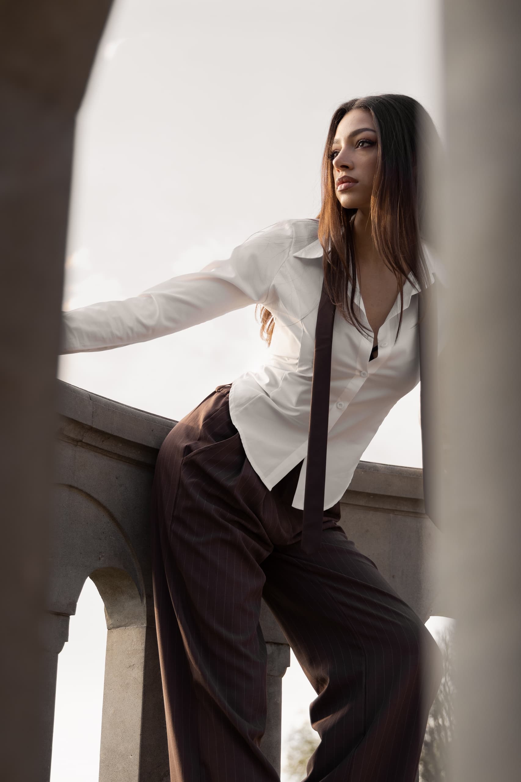 Fashionable woman in white shirt and tie leaning on railing outdoors.