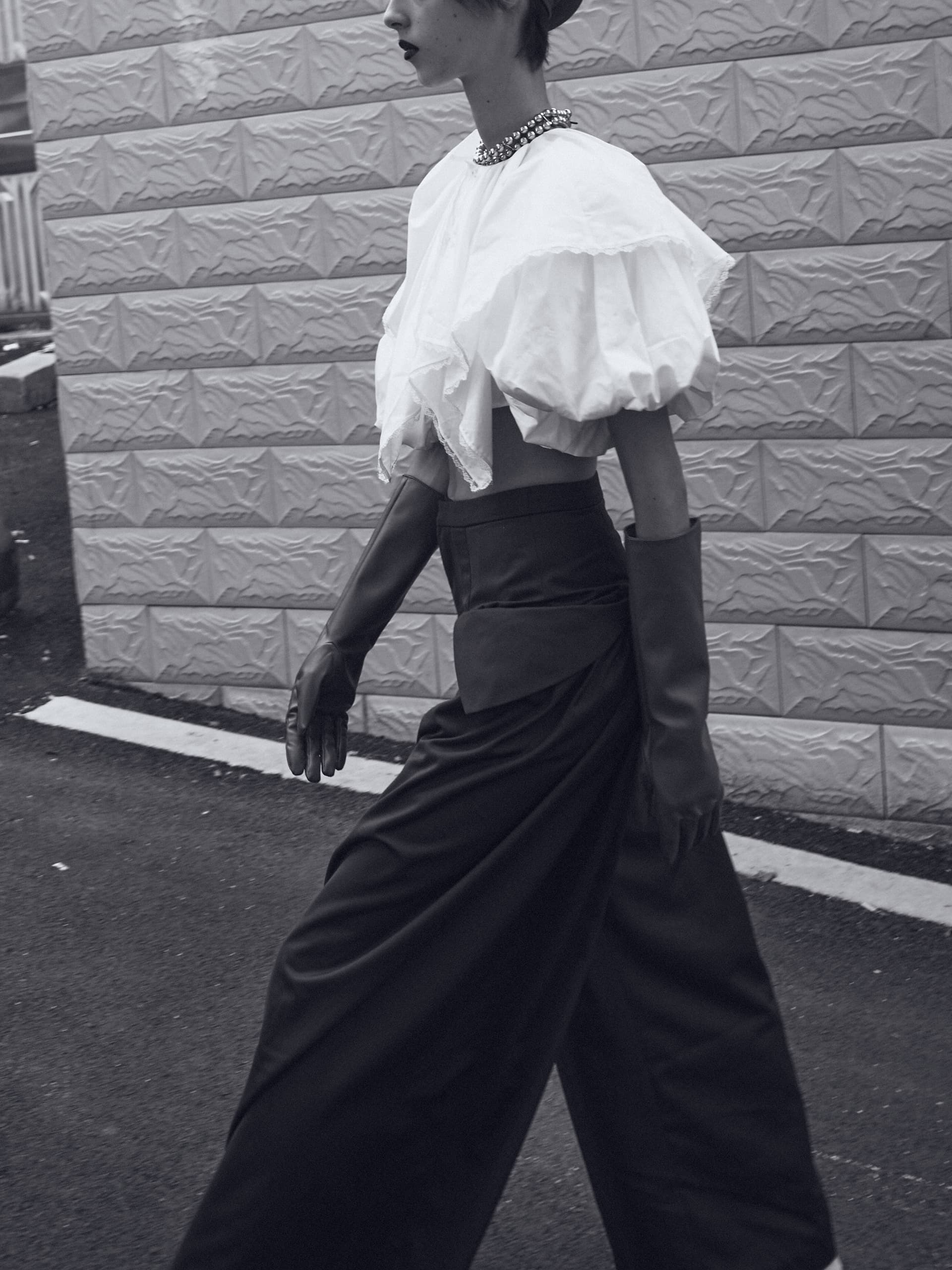 Black and white fashion photo: model in vintage outfit walking beside textured wall.