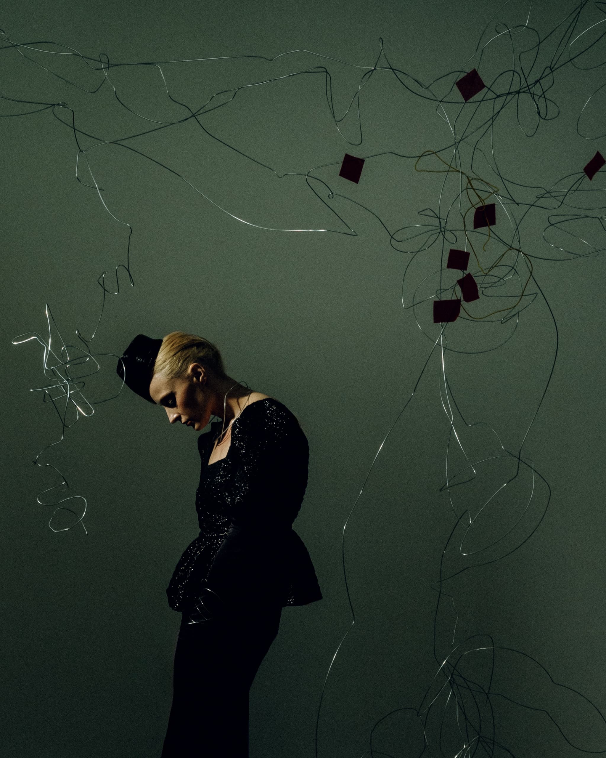 Fashionable woman in elegant black attire with abstract wire art backdrop.