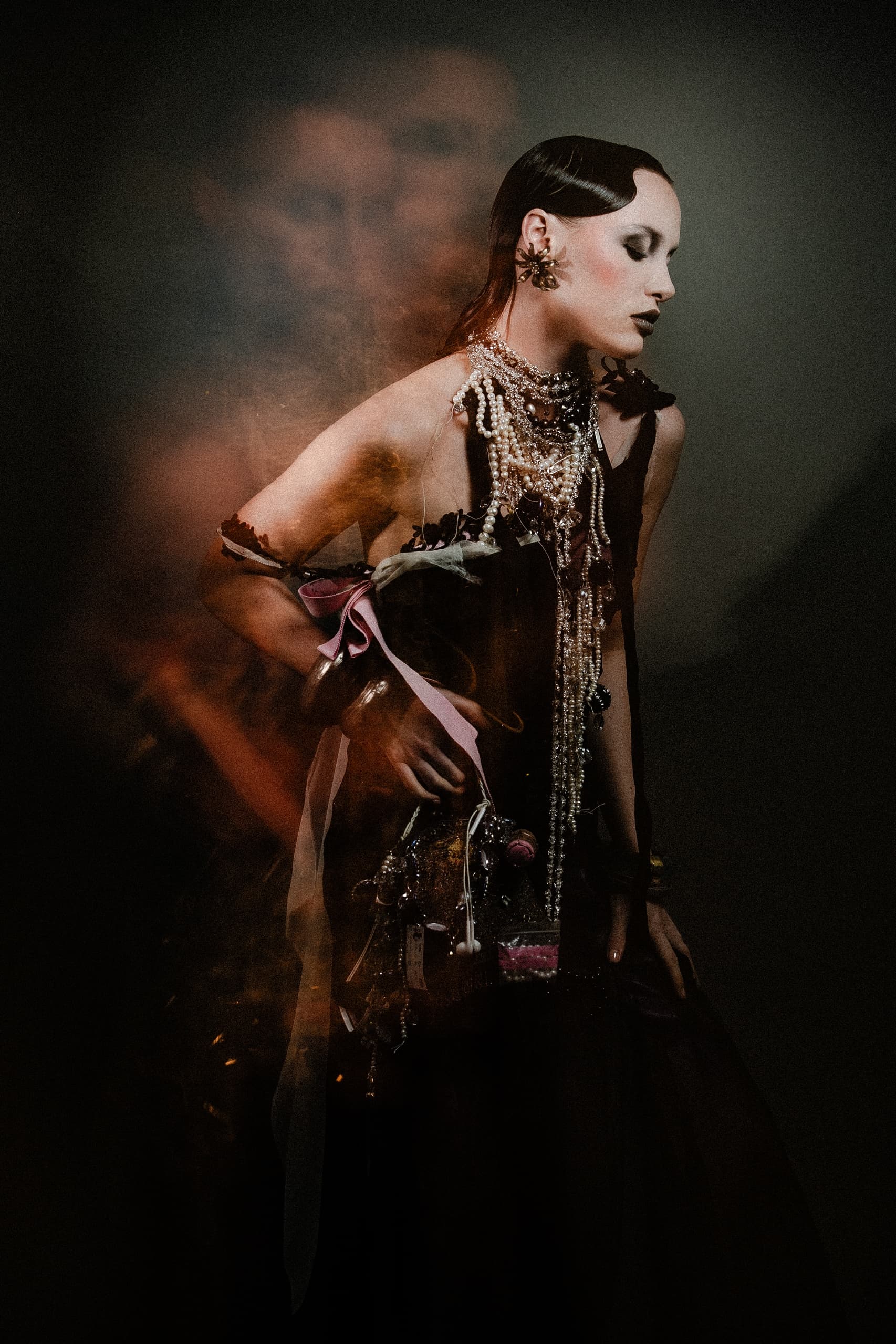 Elegant woman in dark fashion dress adorned with pearls, dramatic lighting.