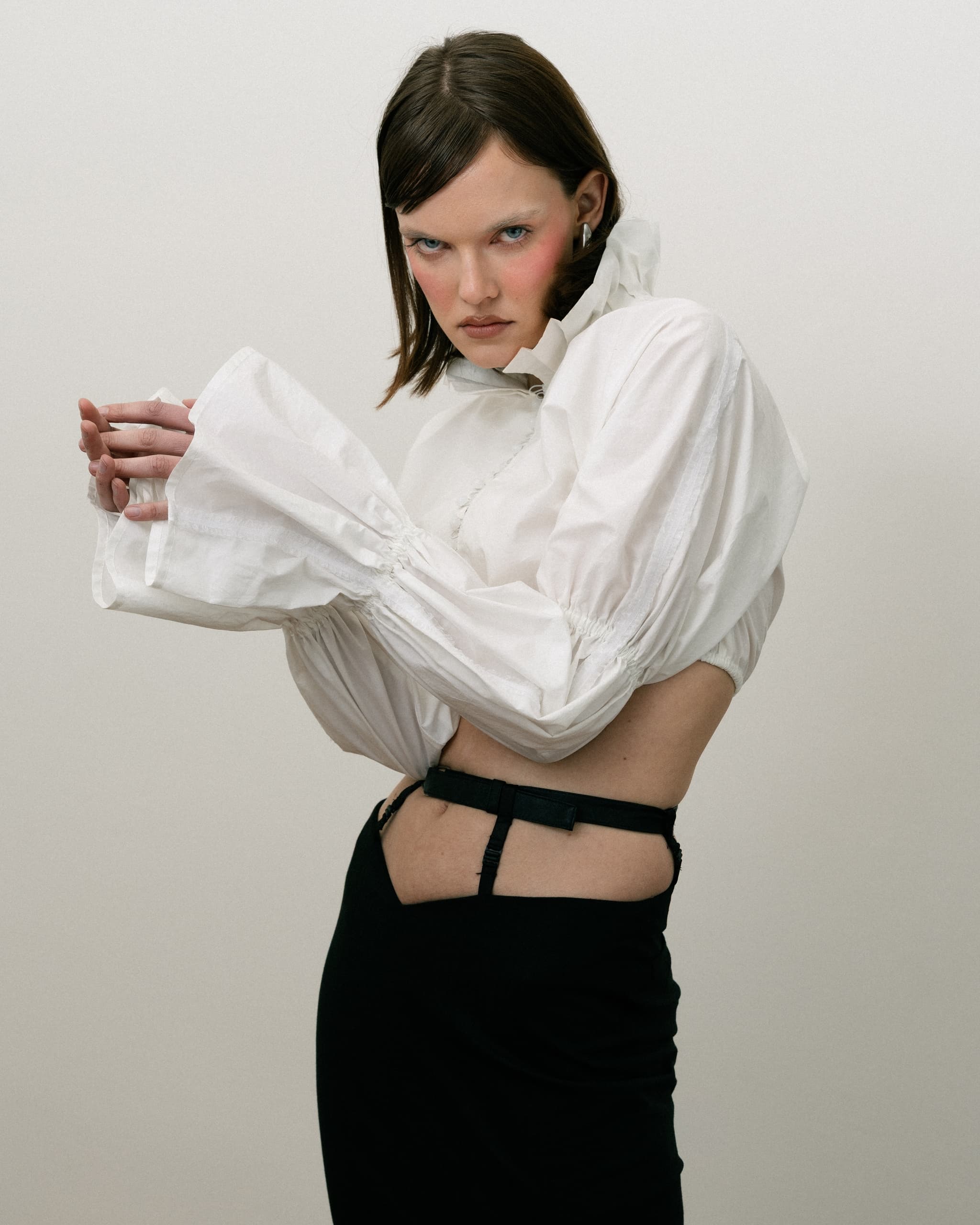 Fashion model in a stylish white blouse and black skirt, posing confidently.