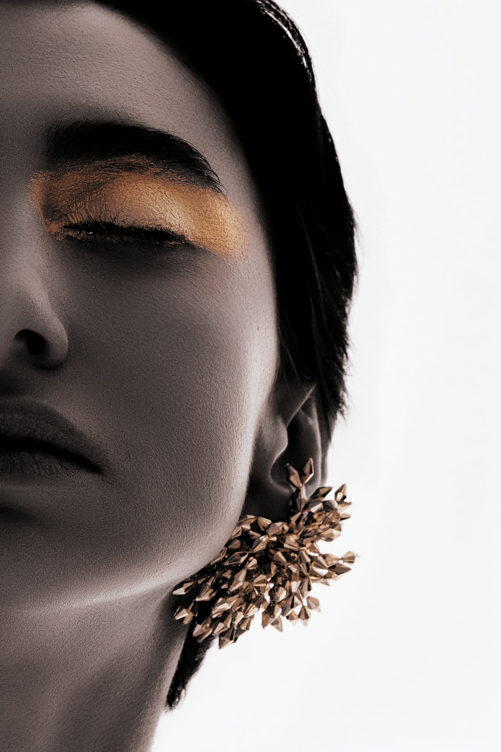 Close-up of a person with gold eyelids and intricate floral earrings.
